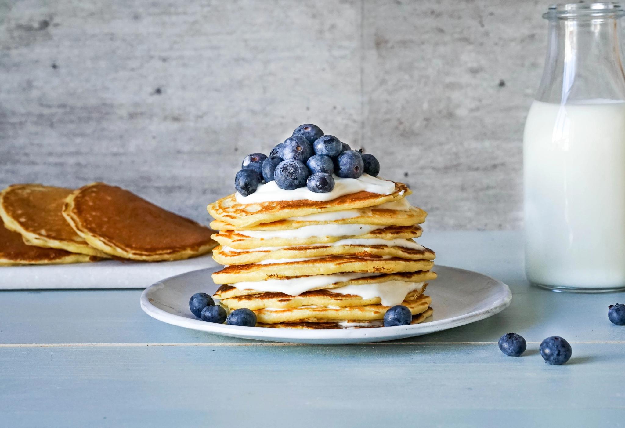 a stack of pancakes with blueberries and whipped cream on a plate next to a bottle of milk .