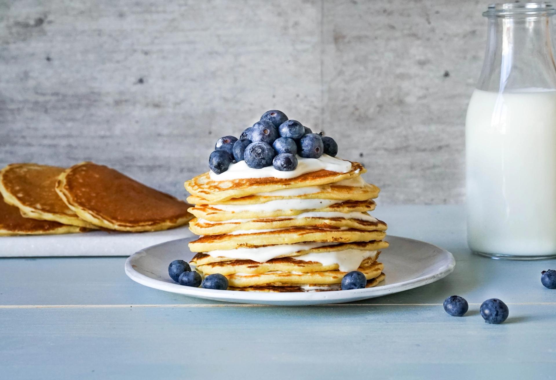 a stack of pancakes with blueberries and whipped cream on a plate next to a bottle of milk .