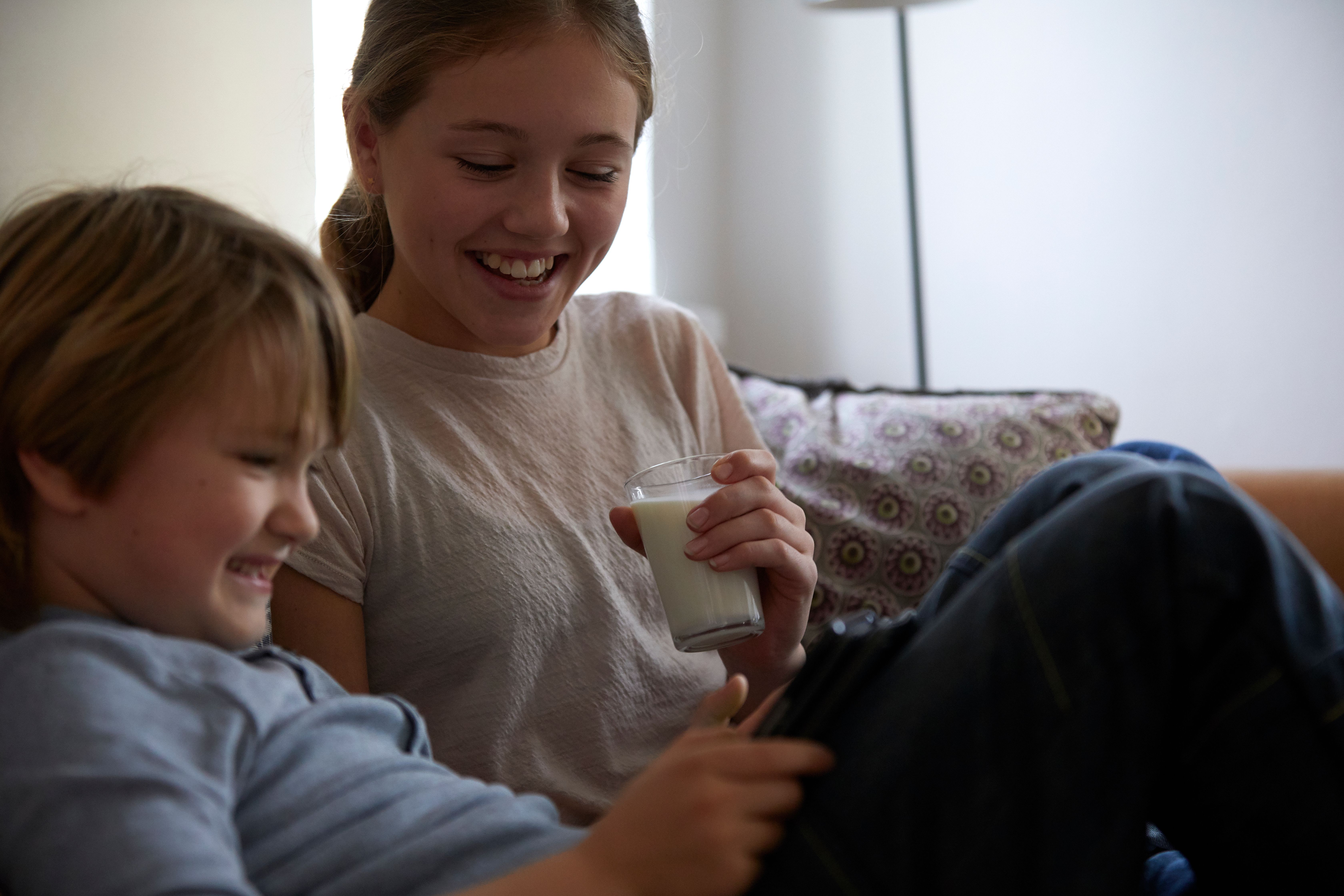 To barn sitter i sofa og drikker melk
