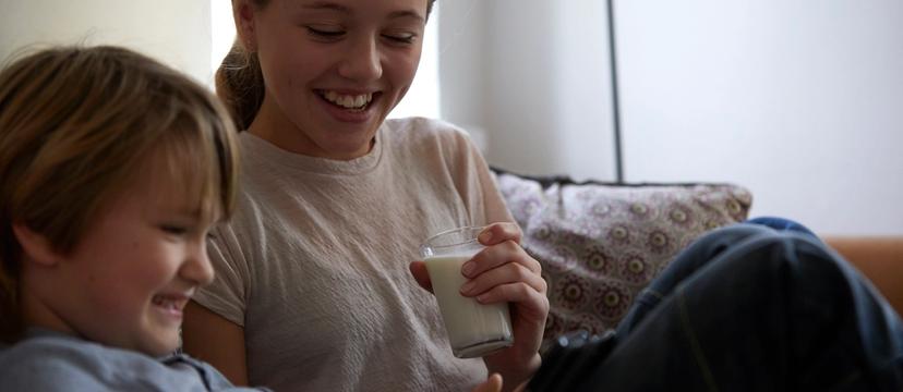 To barn sitter i sofa og drikker melk