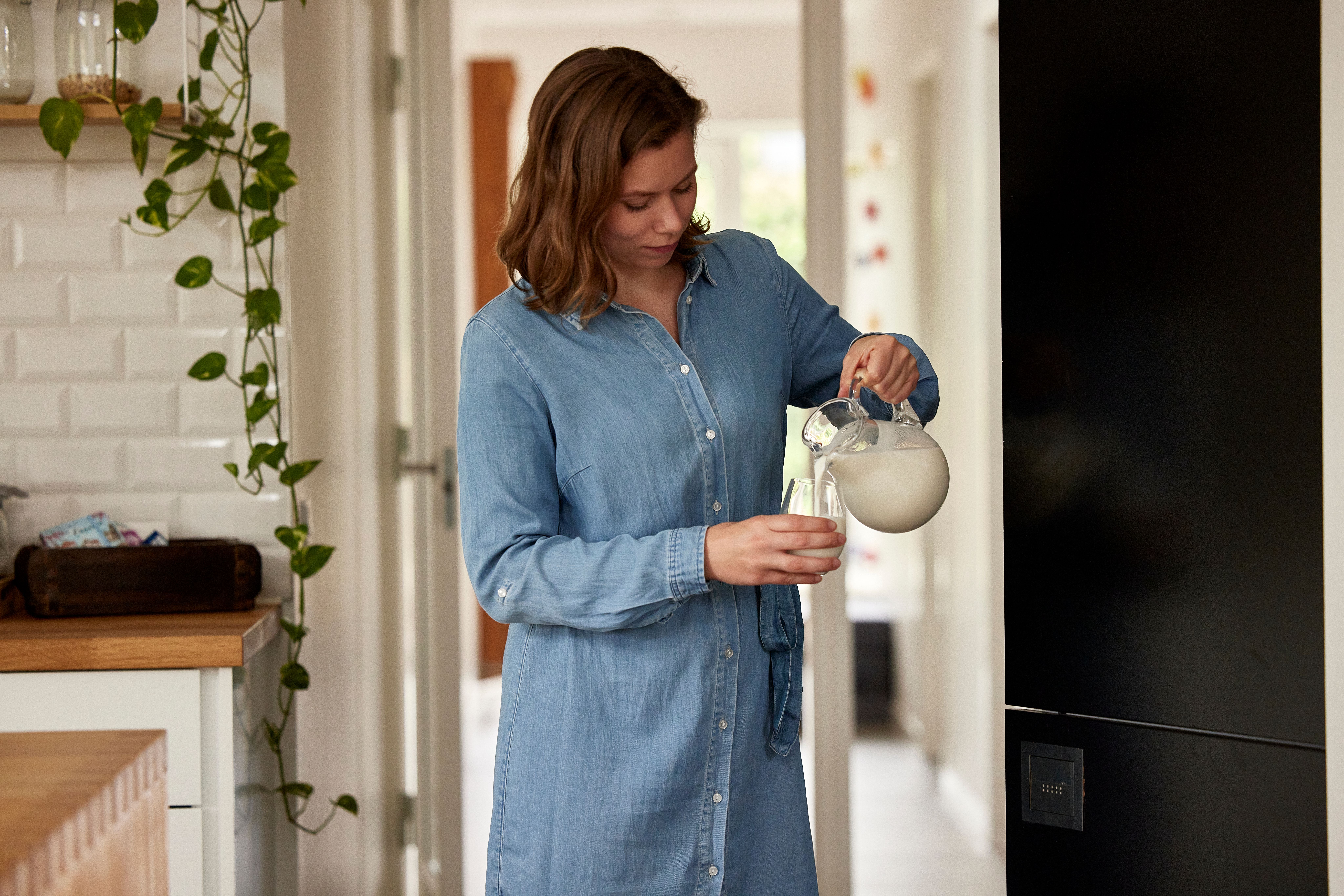 Kvinne heller melk i et glass fra en mugge