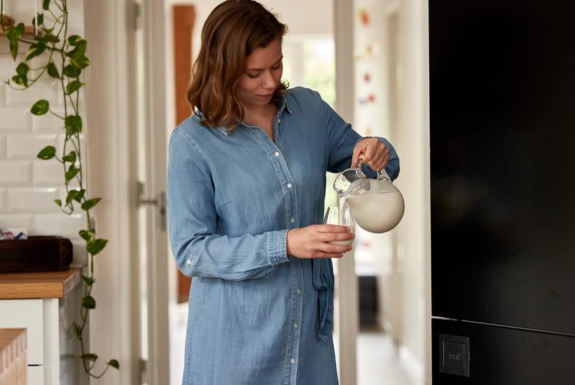 Kvinne heller melk i et glass fra en mugge