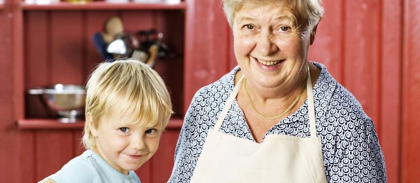 Bestemor som holder opp en kjele med risgrøt, og et barn som rører i grøten med en tresleiv.