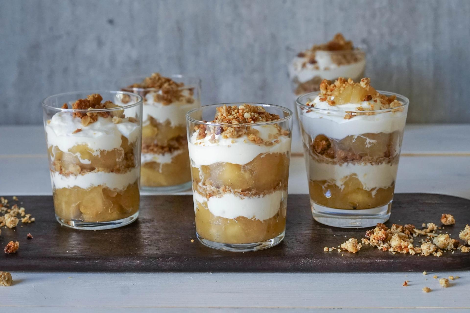 a wooden cutting board topped with four glasses of dessert .