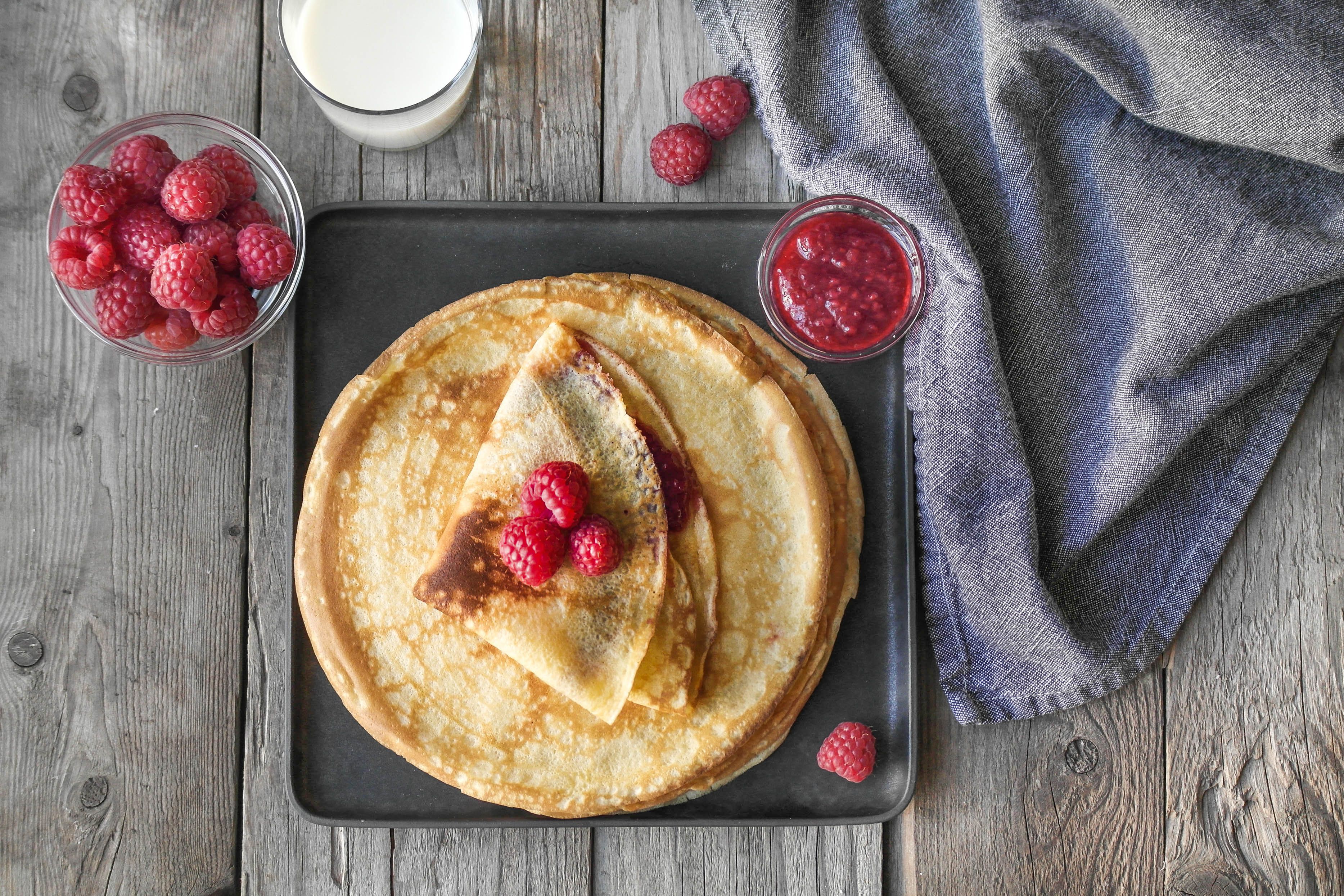 pannekaker toppet med bringebær og et glass melk