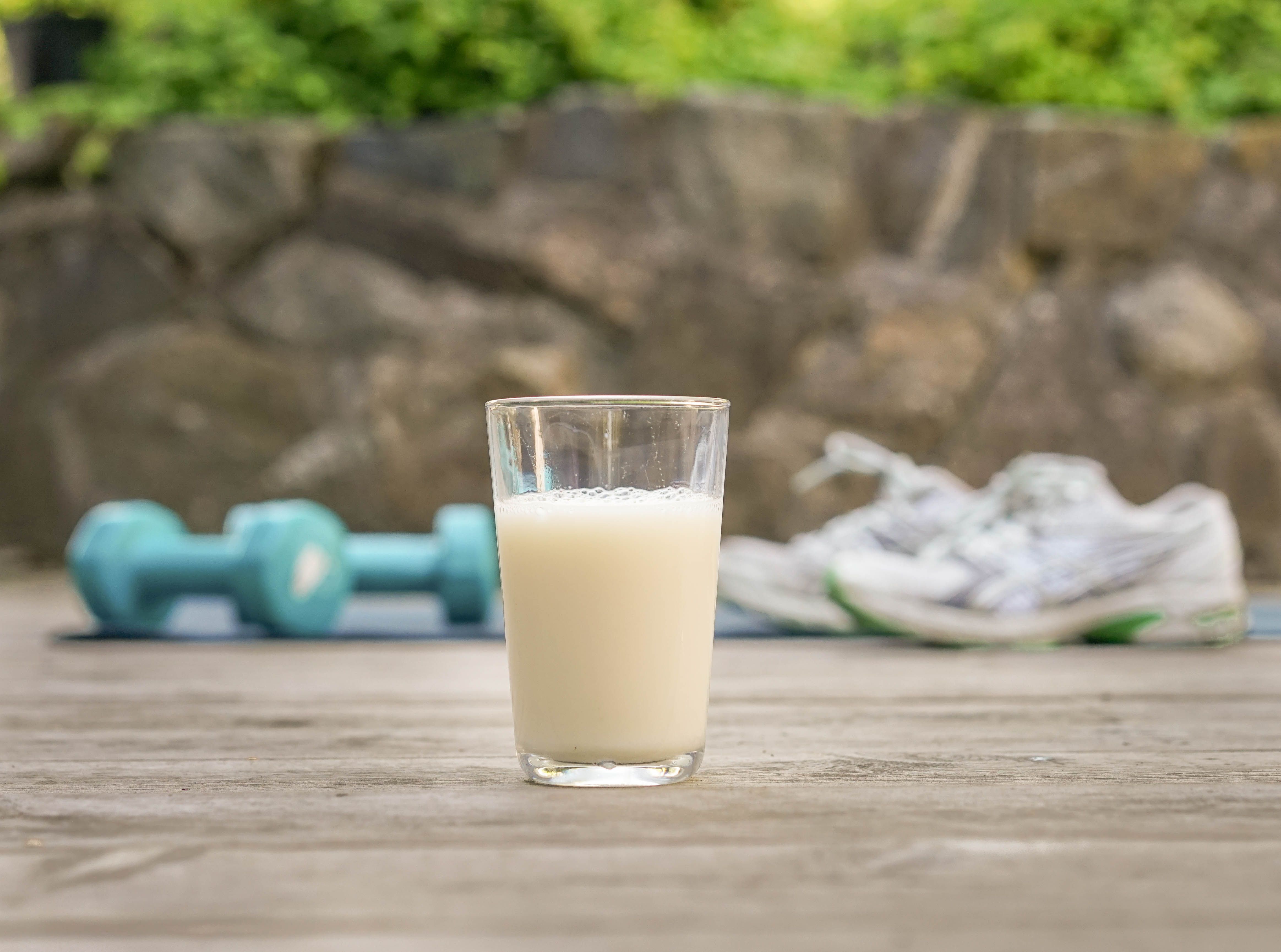 a glass of milk is sitting on a wooden table next to a pair of shoes and dumbbells .