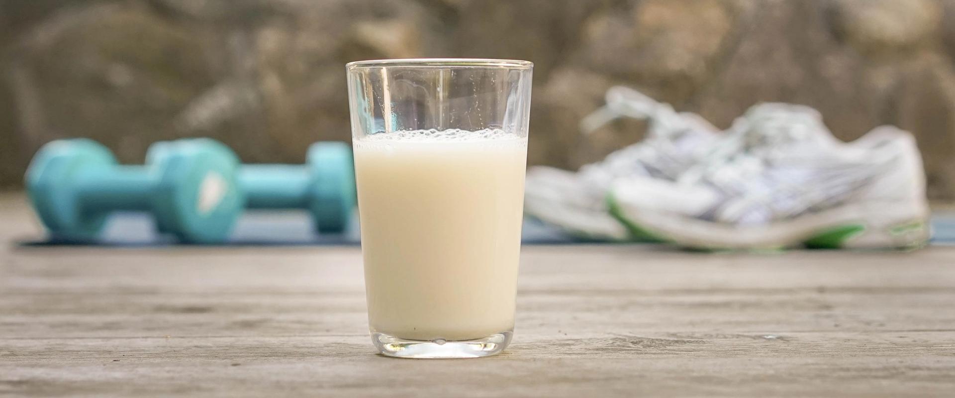 a glass of milk is sitting on a wooden table next to a pair of shoes and dumbbells .