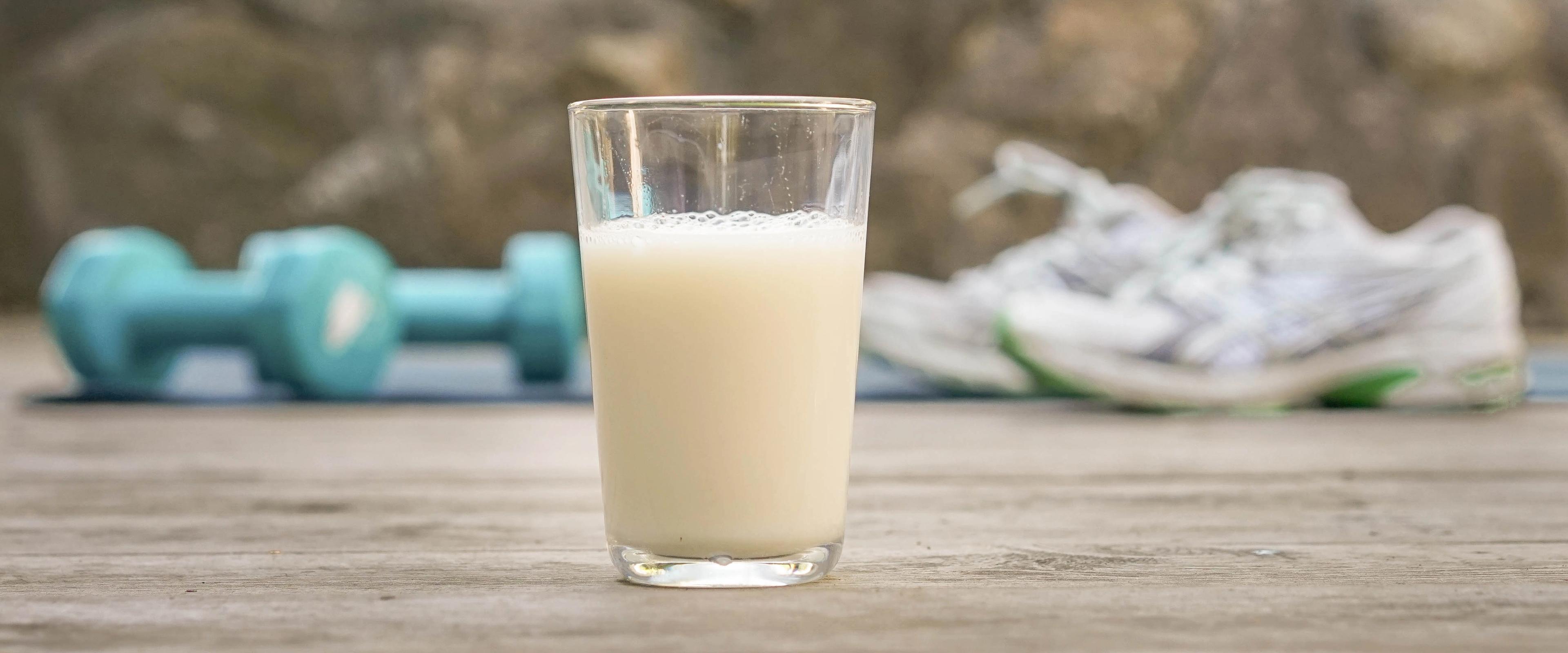 a glass of milk is sitting on a wooden table next to a pair of shoes and dumbbells .