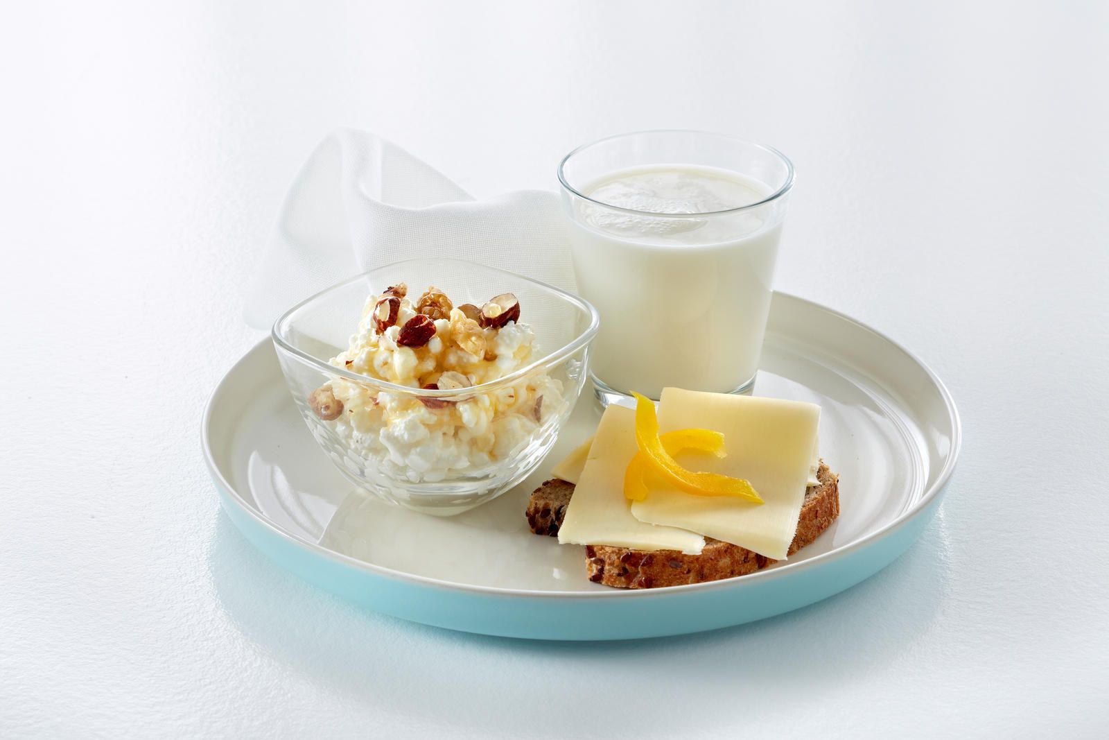 Fat med cottage cheese med syltetøy, en brødskive med gulost og gul paprika og et glass melk.