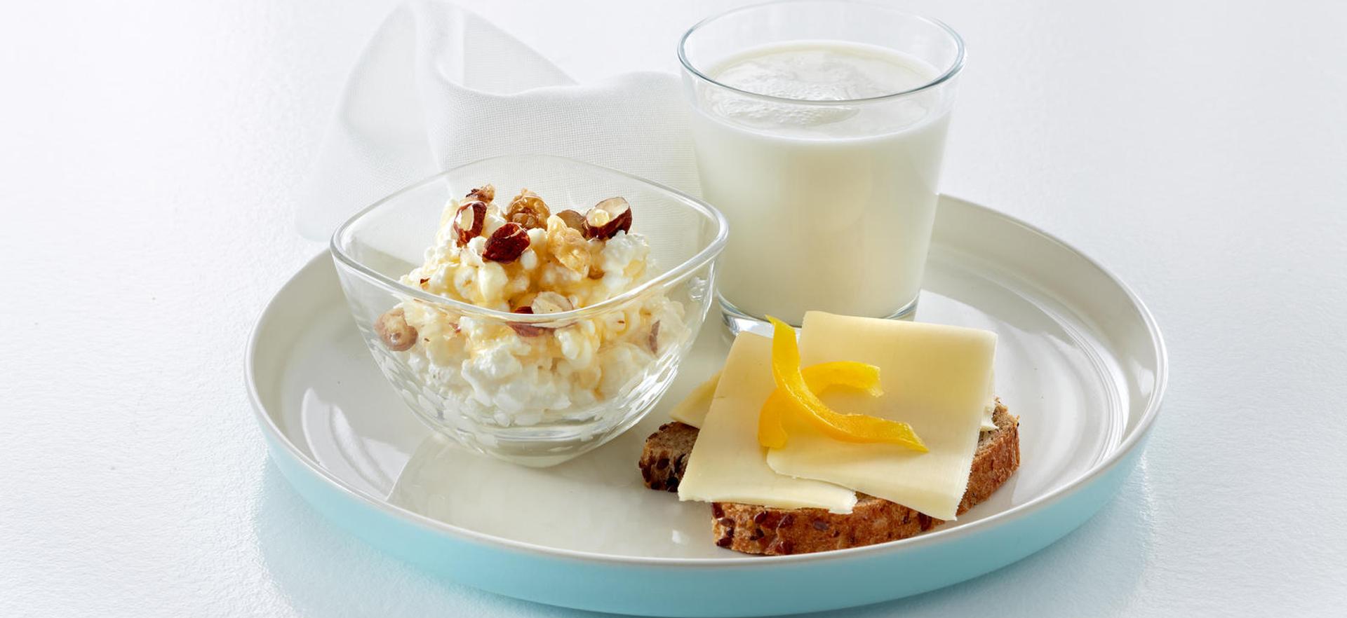 Fat med cottage cheese med syltetøy, en brødskive med gulost og gul paprika og et glass melk.