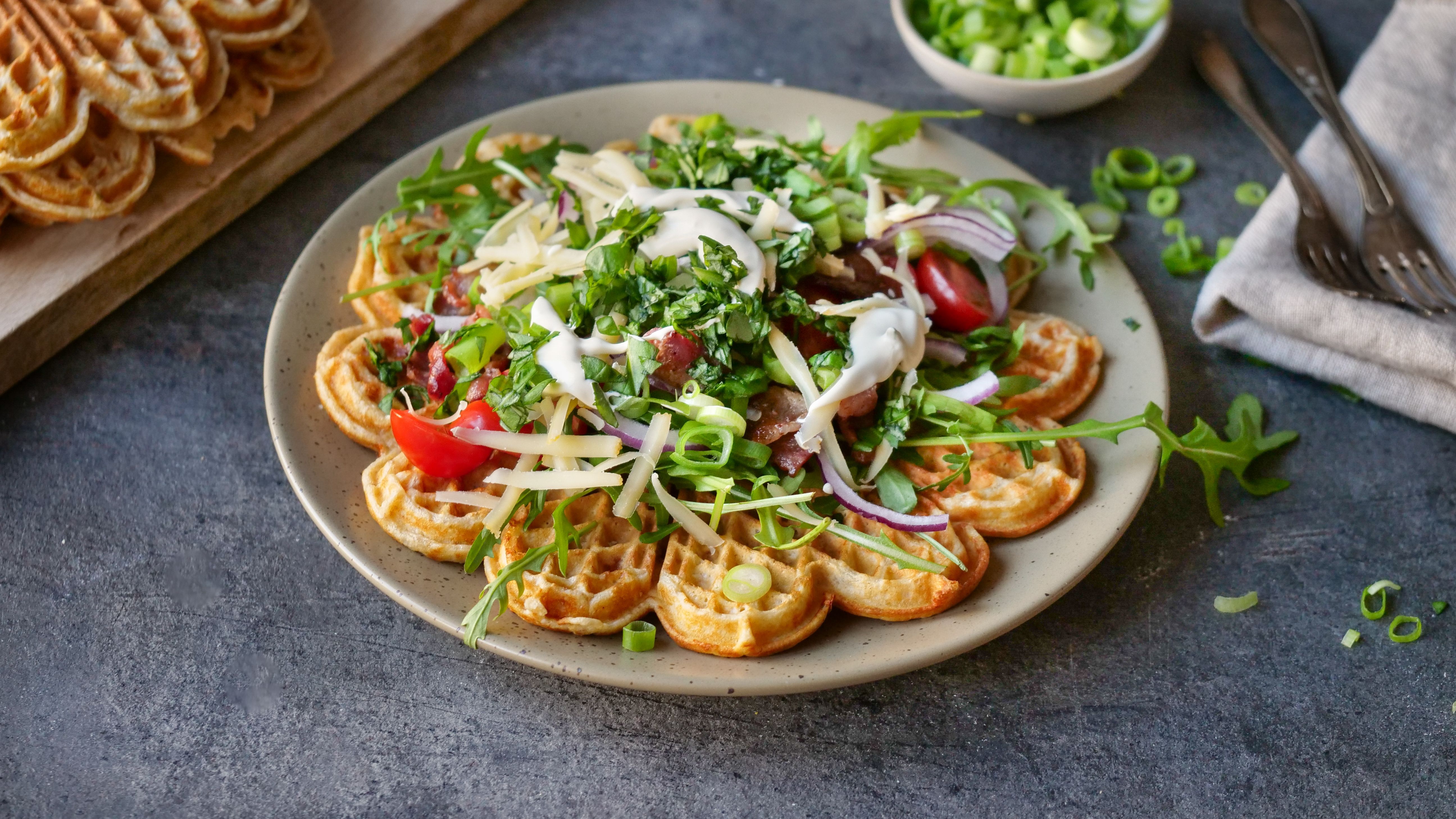 Vafler på tallerken toppet med bacon, ost og grønnsaker 
