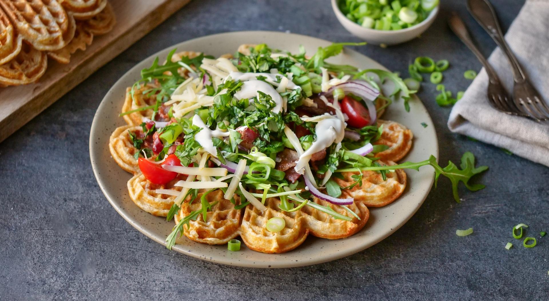 Vafler på tallerken toppet med bacon, ost og grønnsaker