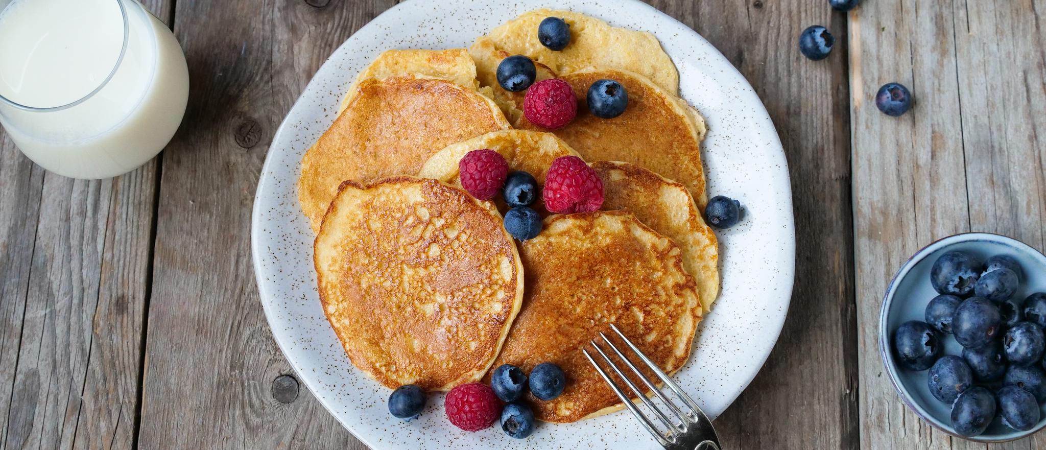 a plate of pancakes with berries and a glass of milk on a wooden table .