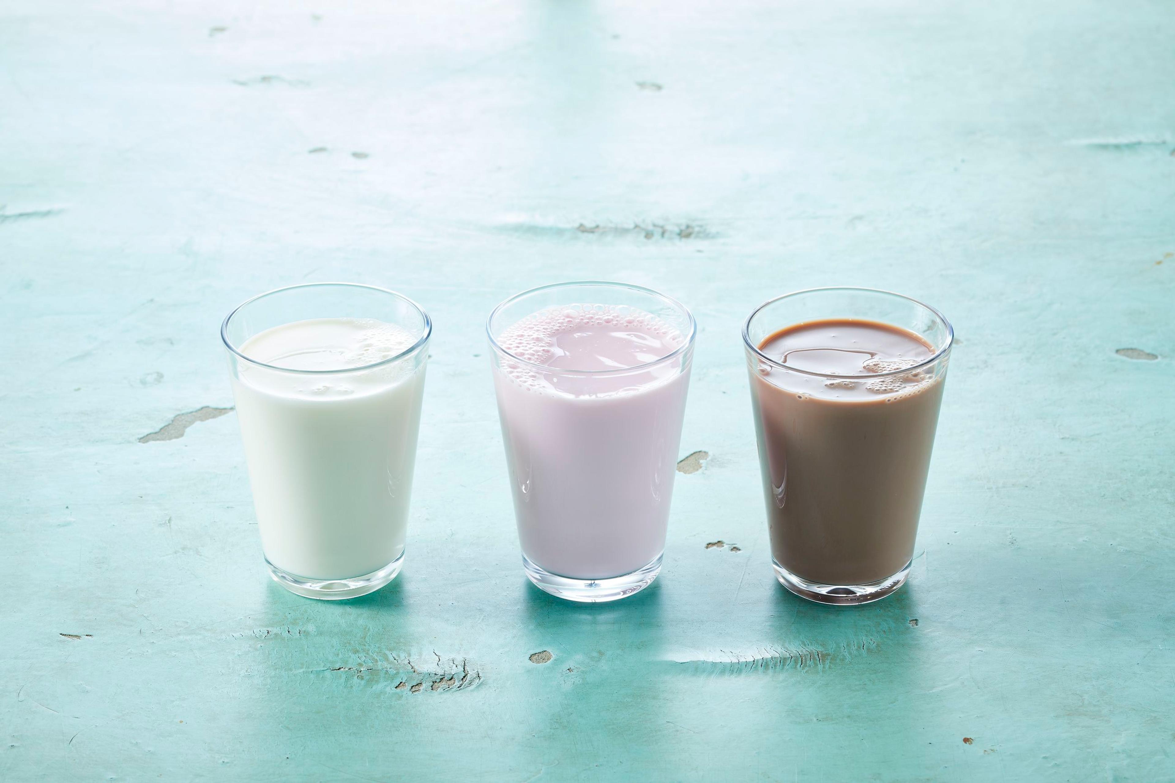 three glasses of different types of milk are sitting on a table .