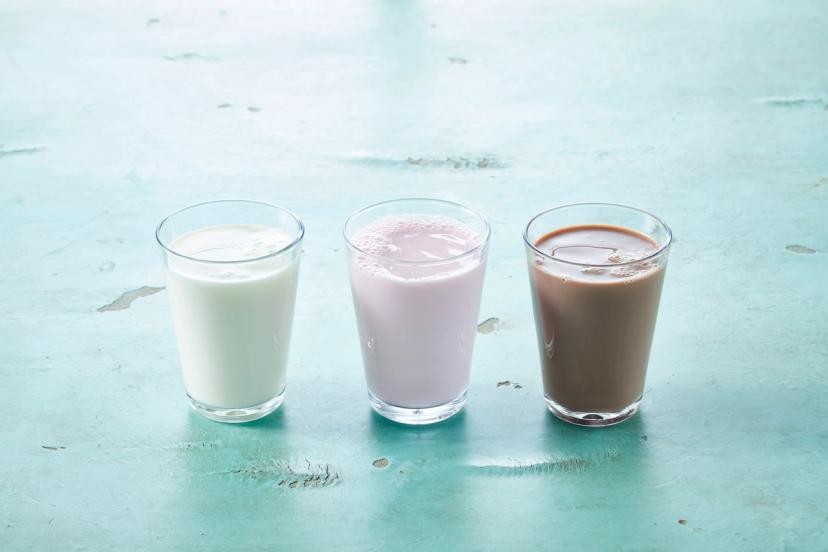 three glasses of different types of milk are sitting on a table .