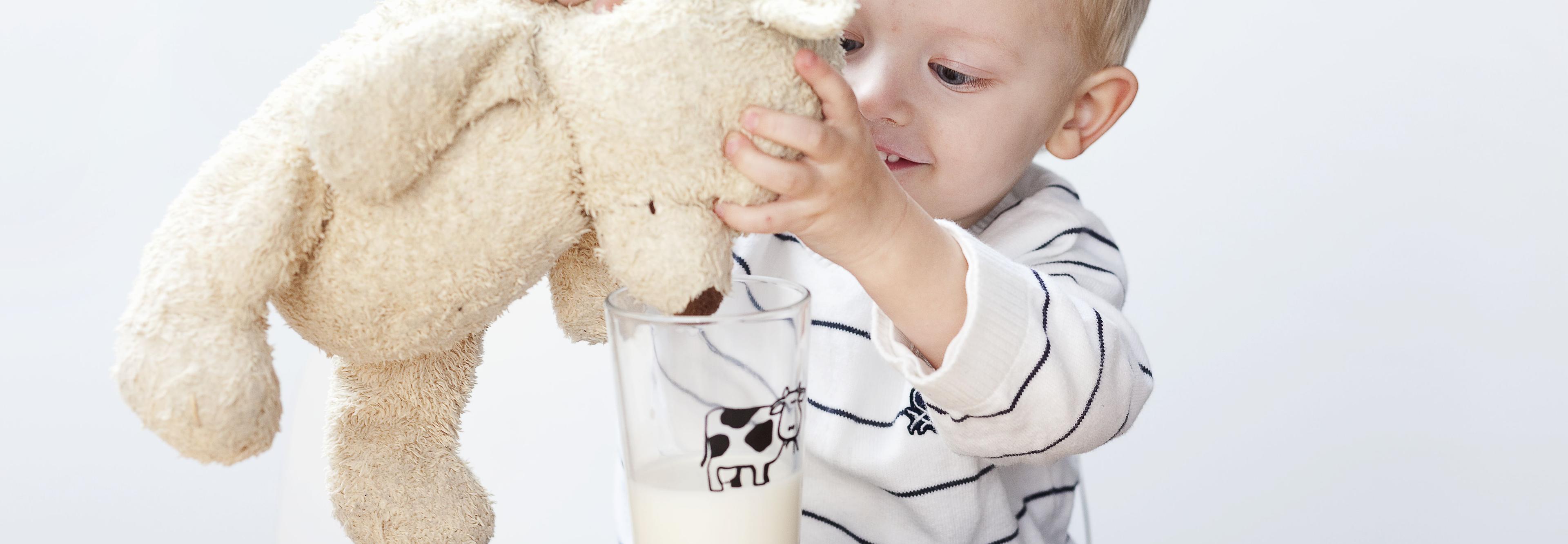Liten gutt som gir en lysebrun bamse melk fra et glass.