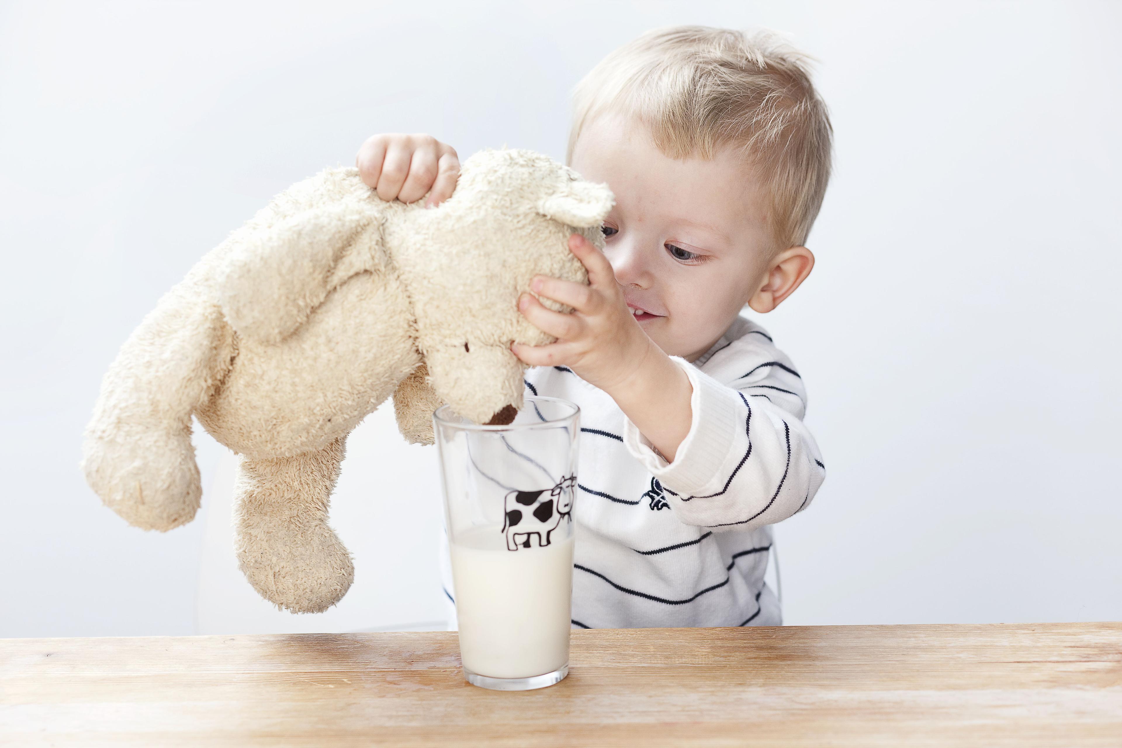 Liten gutt som gir en lysebrun bamse melk fra et glass.