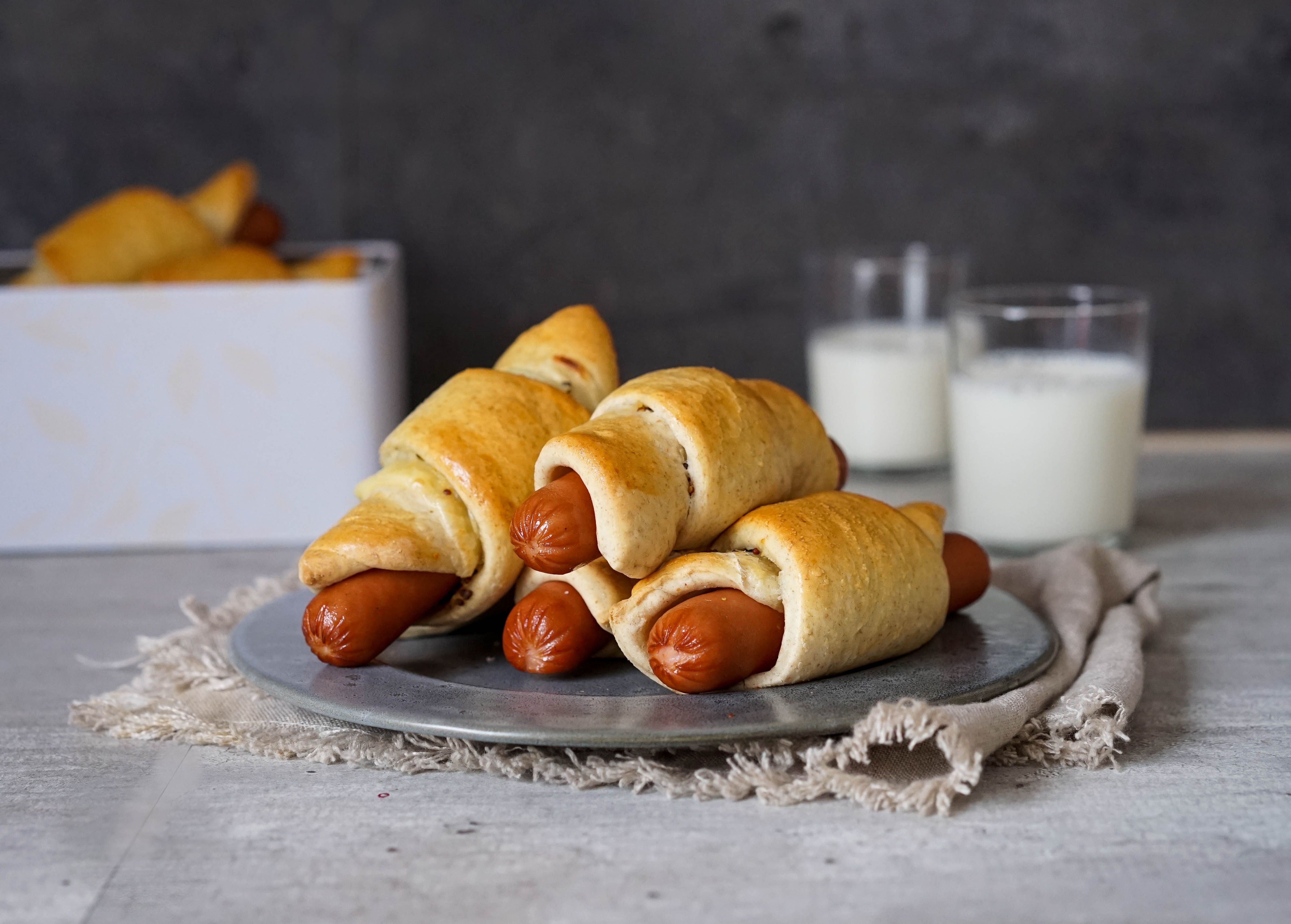 Fire pølsehorn på en tallerken med to glass melk i bakgrunnen
