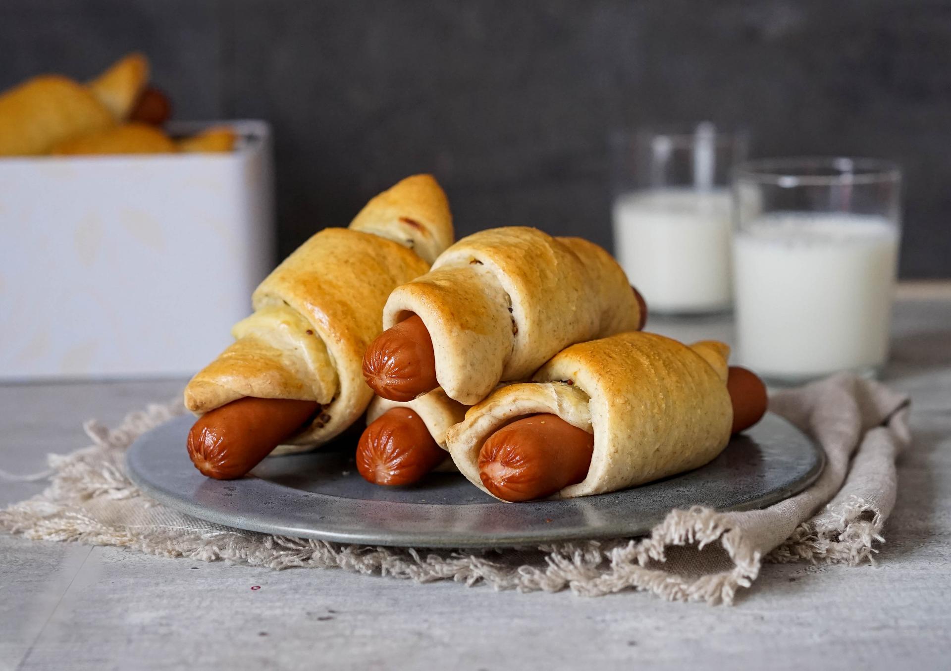 Fire pølsehorn på en tallerken med to glass melk i bakgrunnen