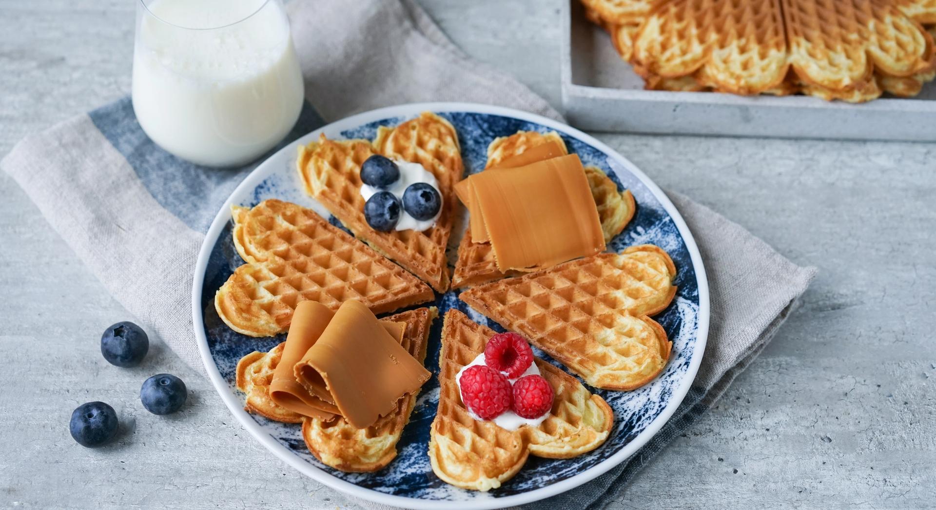 a plate of waffles with raspberries , cheese and a glass of milk .