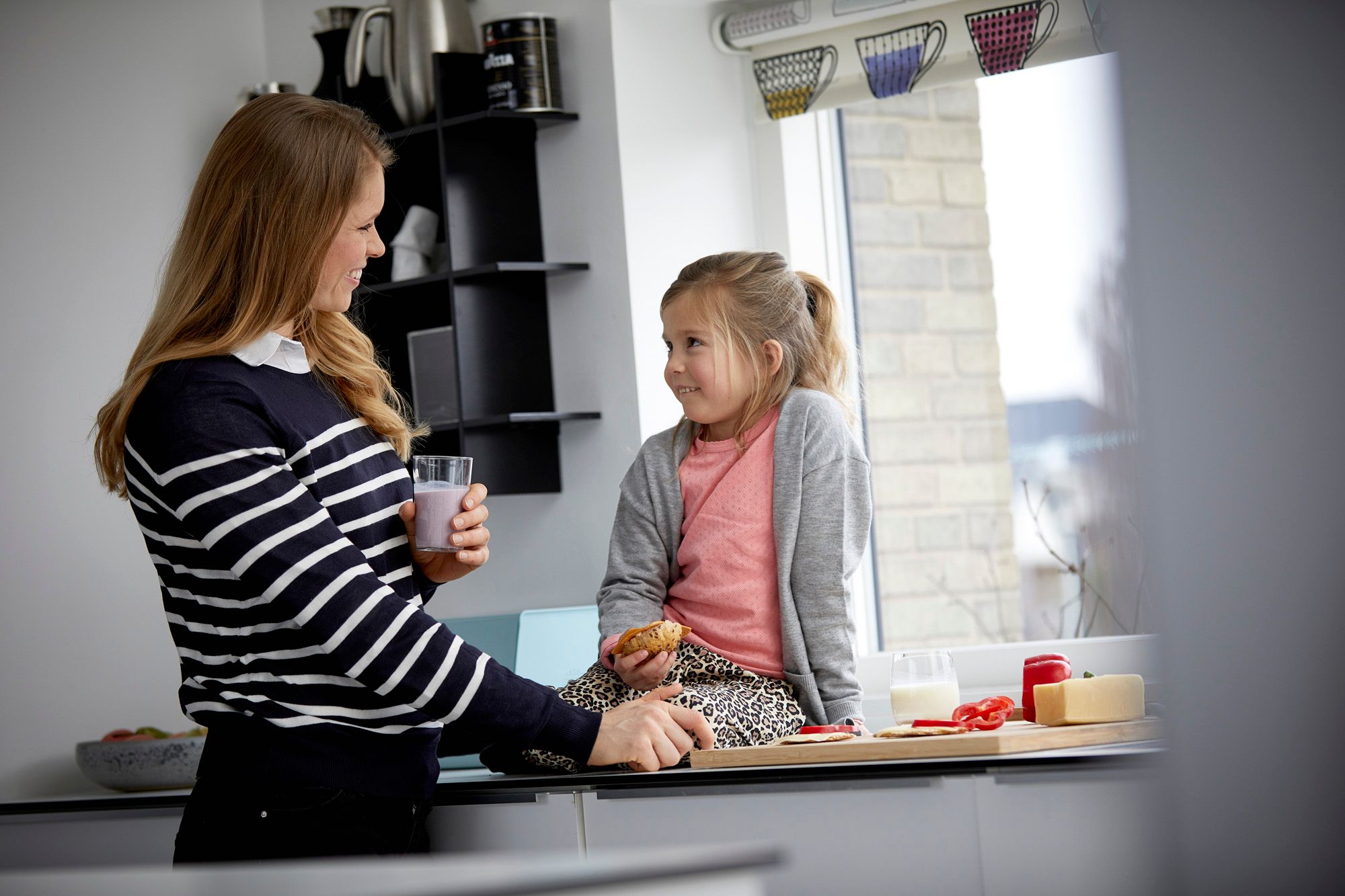 Mor med melkeglass og datter med rundstykke med brunost