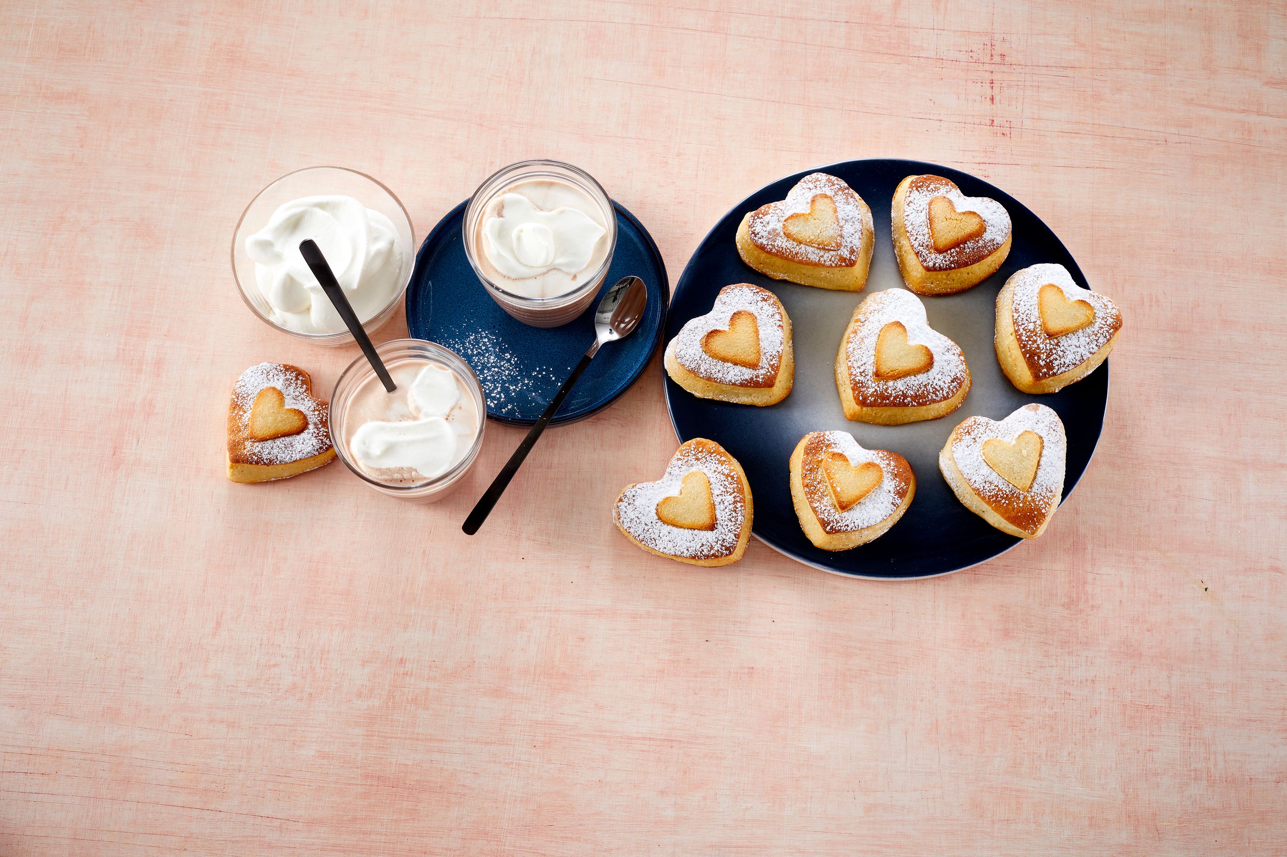 Hjerteboller på en stor tallerken ved siden av to glass kakao med krem