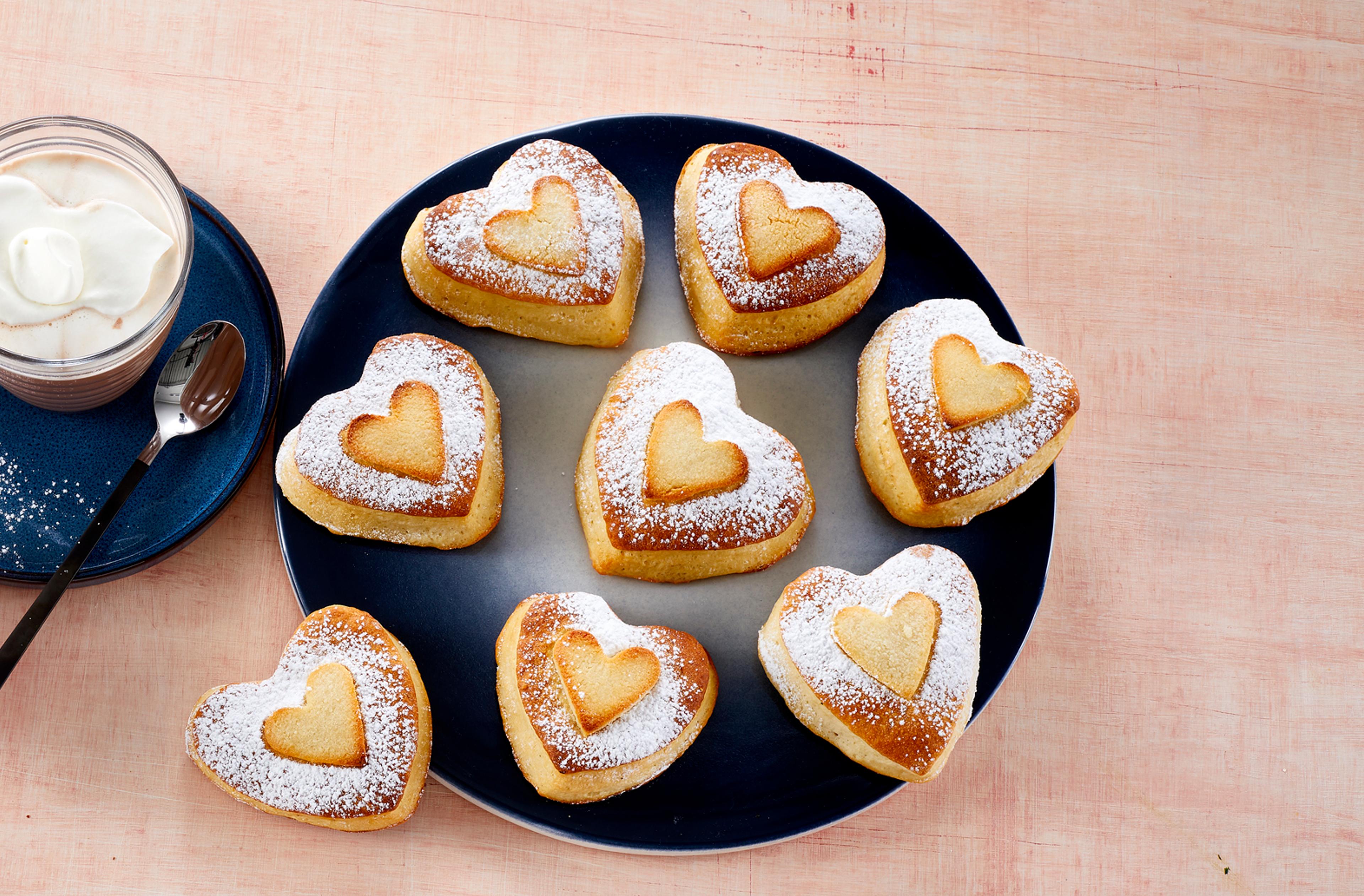 Hjerteboller på en stor tallerken ved siden av to glass kakao med krem