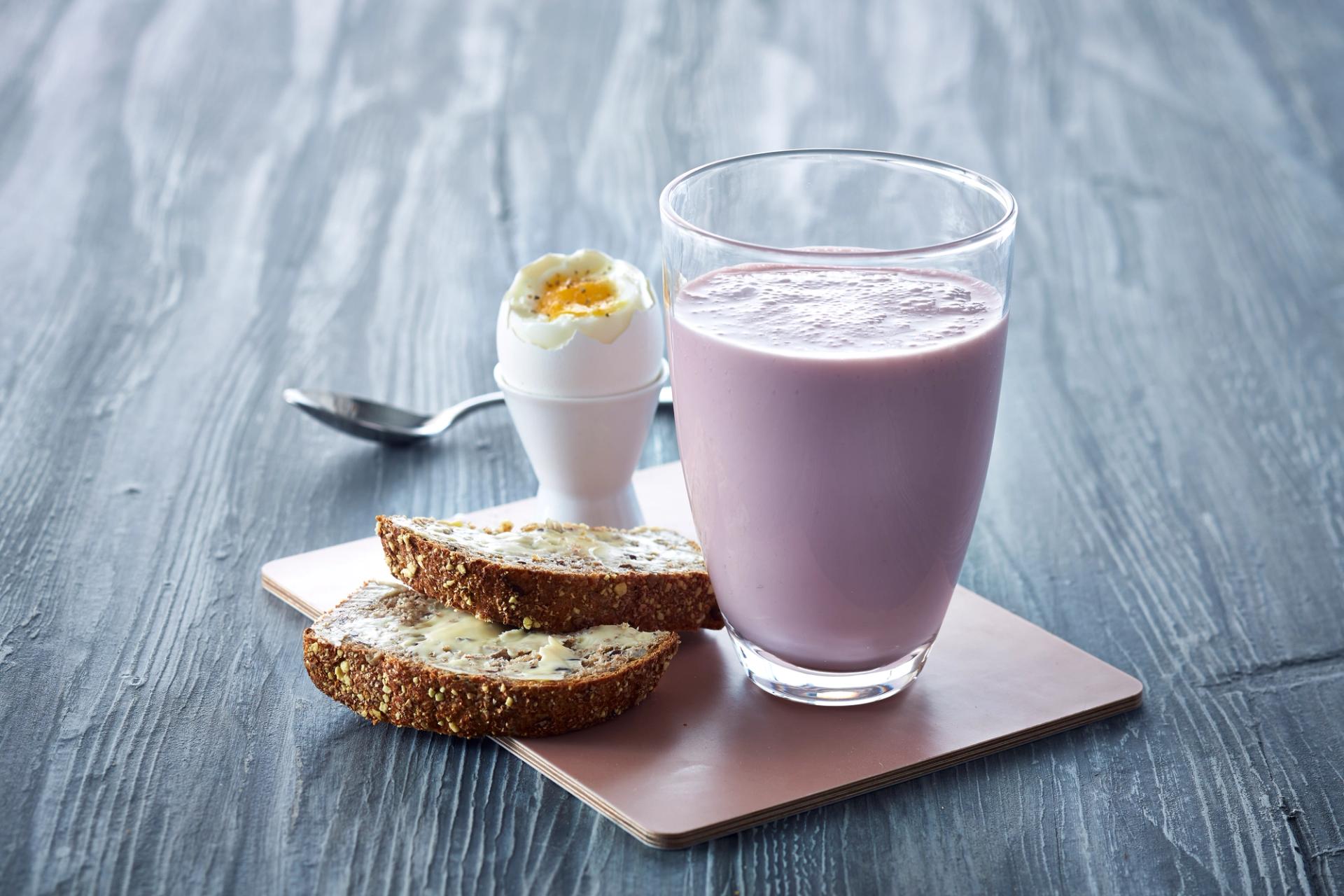 Syrnet melk med bringebær i glass ved siden av et egg og to brødskiver