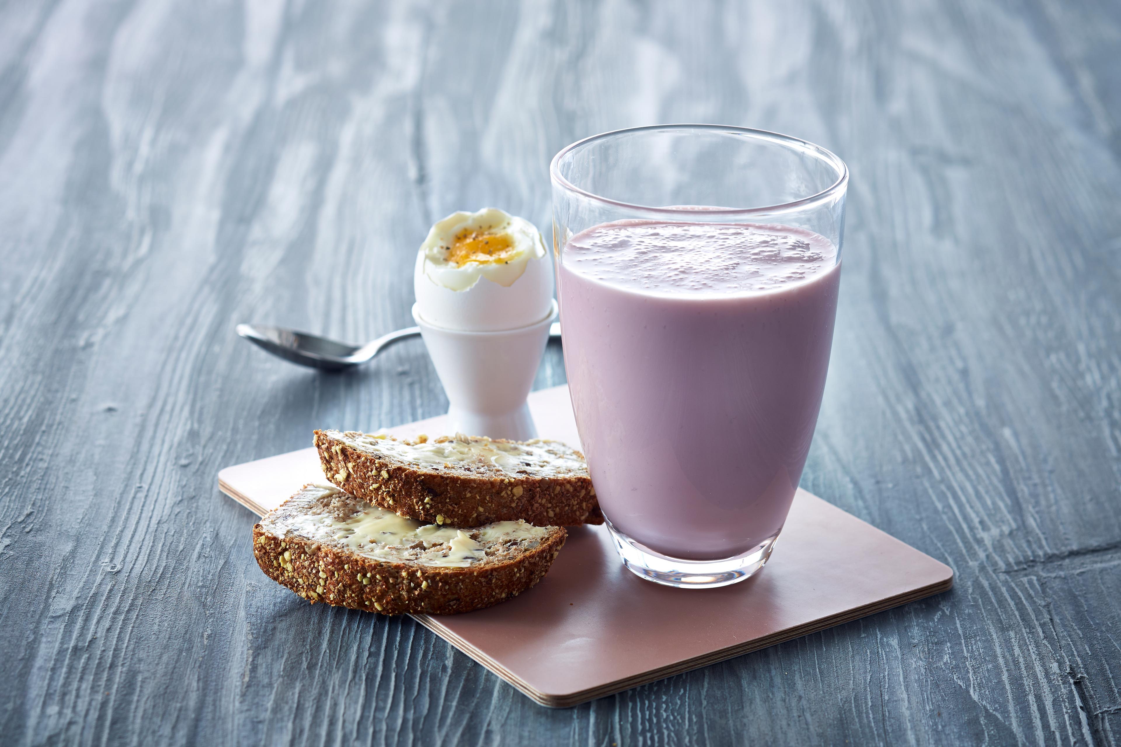 Syrnet melk med bringebær i glass ved siden av et egg og to brødskiver