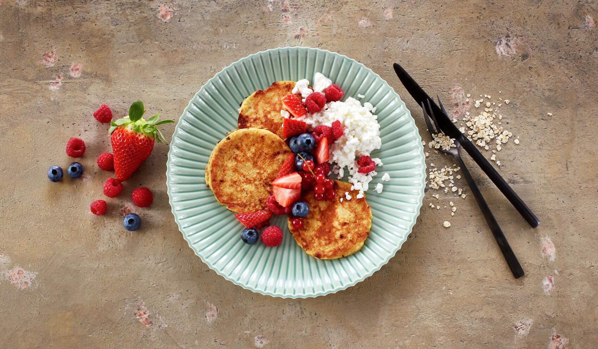 Små pannekaker på en tallerken, toppet med bringebær, blåbær og cottage cheese