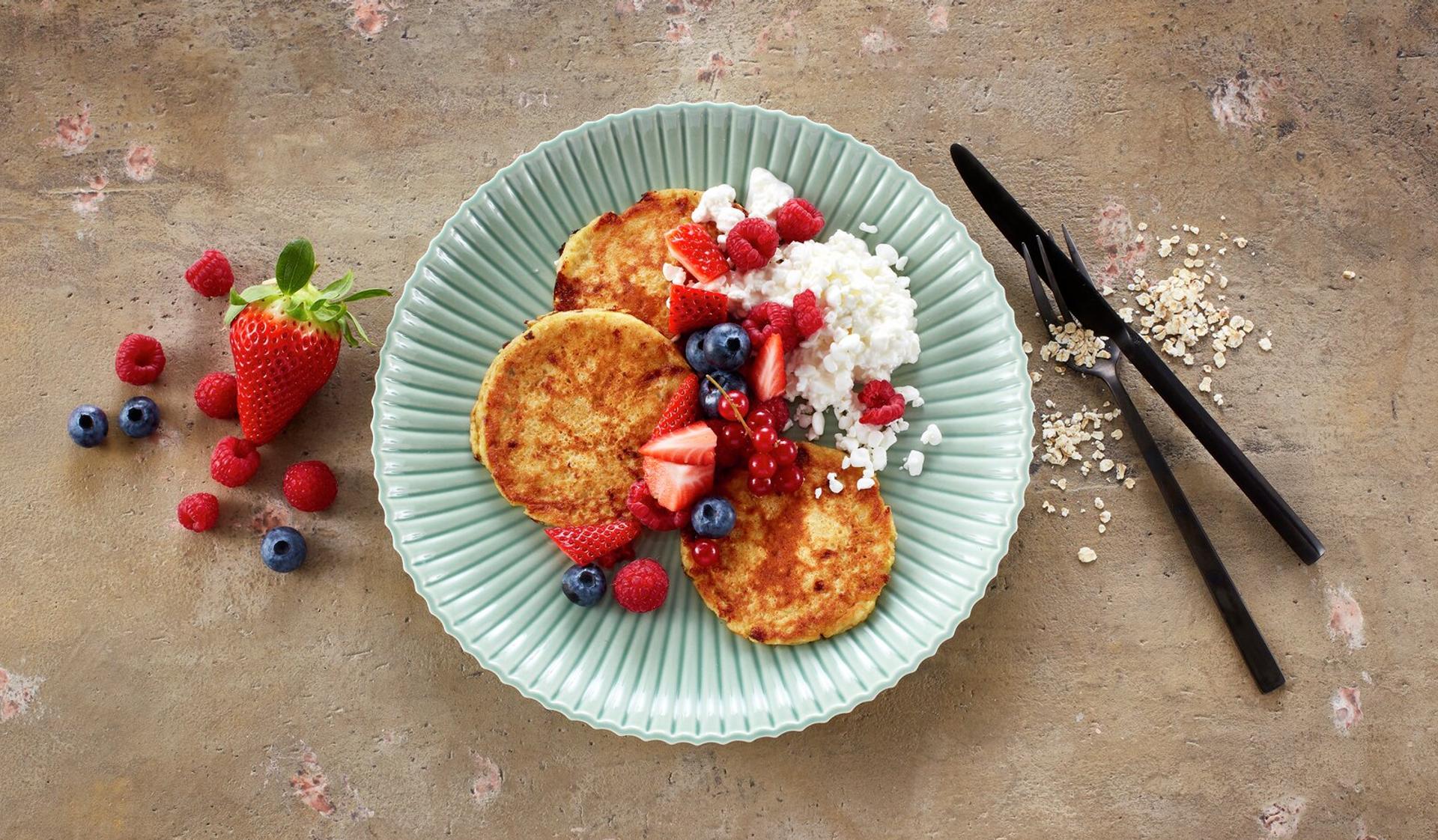 Tallerken med små pannekaker, toppet med bringebær, blåbær og cottage cheese