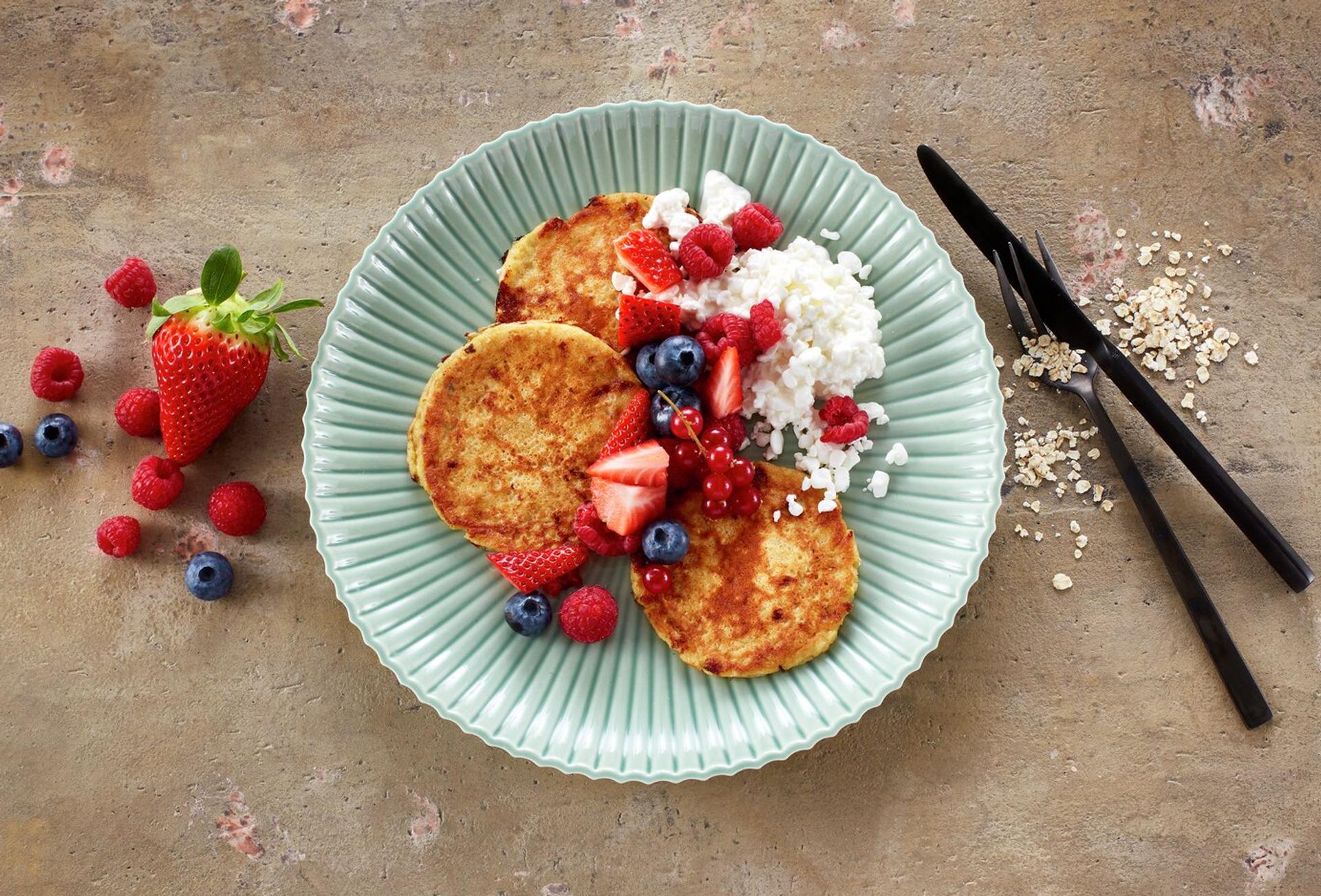 Tallerken med små pannekaker toppet med bringebær, blåbær og cottage cheese