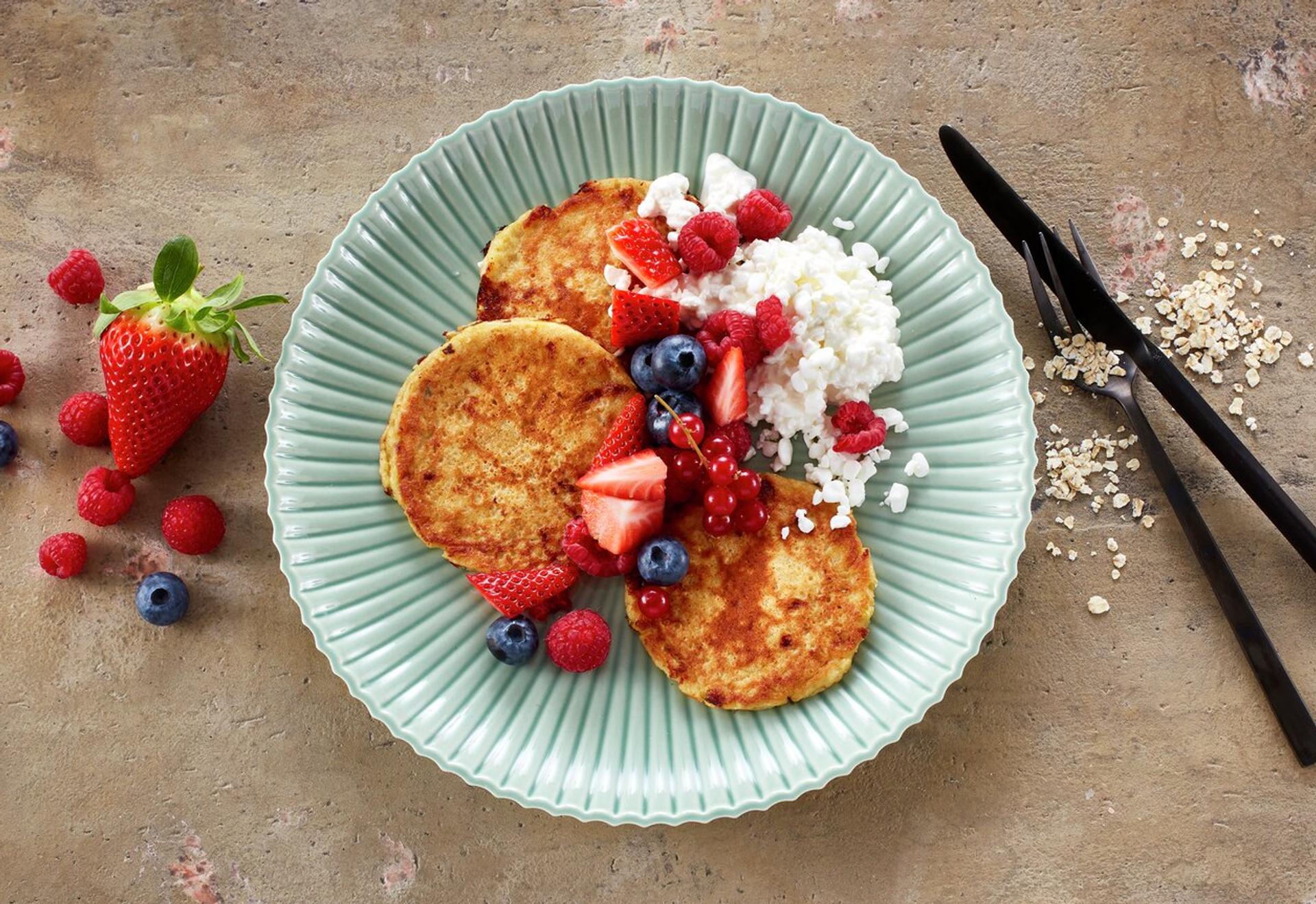 Små pannekaker på tallerken, toppet med cottage cheese, jordbær og blåbær