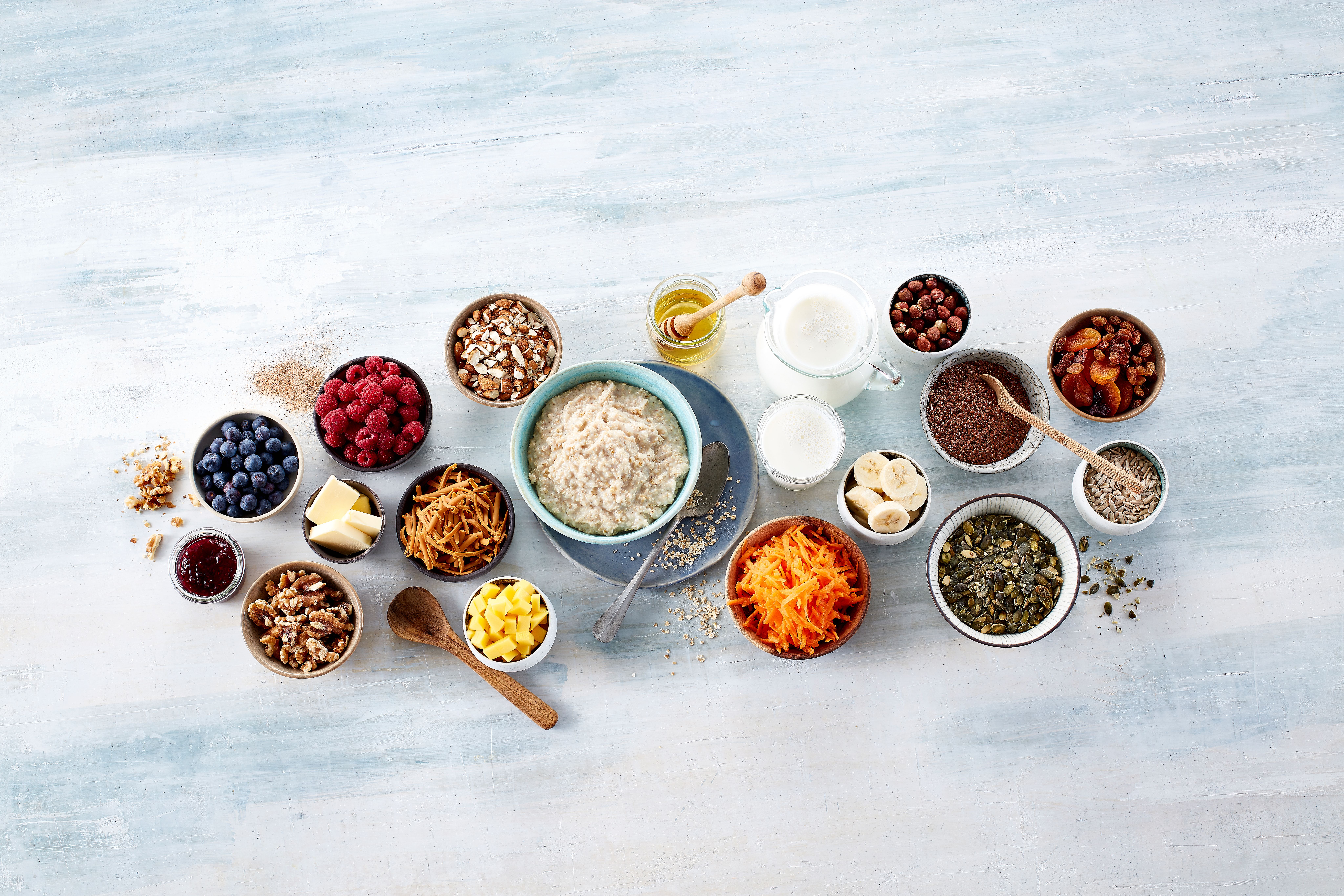 Tallerken med havregrøt og mange skåler med topping som nøtter,  tørket frukt, oppskåret frukt og bær.