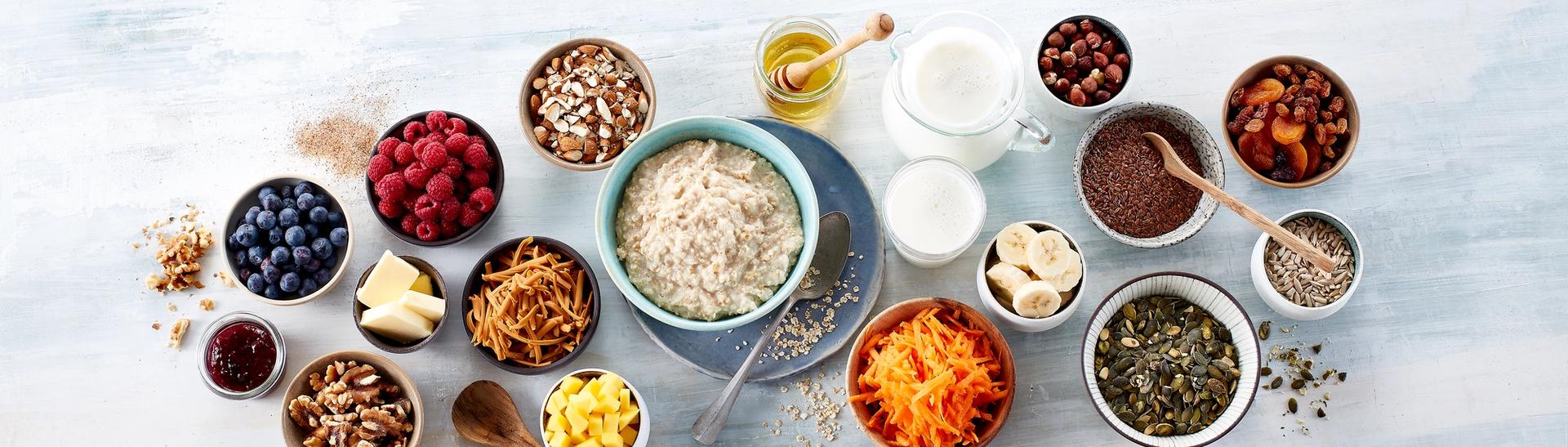 Tallerken med havregrøt og mange skåler med topping som nøtter, tørket frukt, oppskåret frukt og bær.