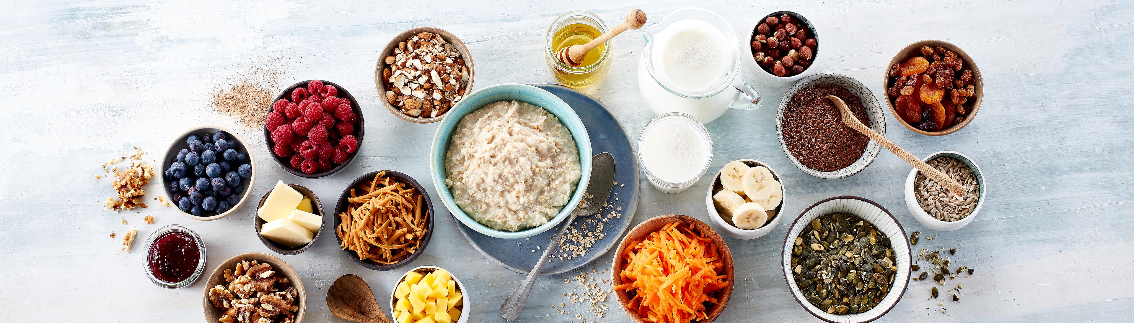 Tallerken med havregrøt og mange skåler med topping som nøtter,  tørket frukt, oppskåret frukt og bær.