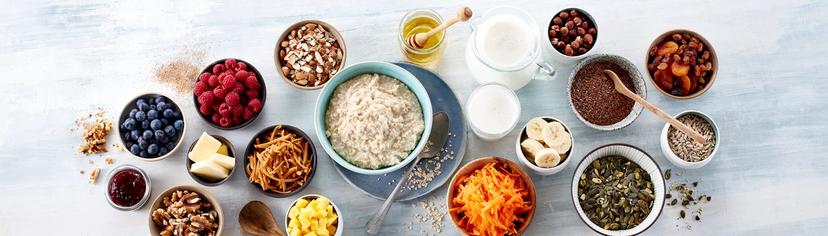 Tallerken med havregrøt og mange skåler med topping som nøtter,  tørket frukt, oppskåret frukt og bær.