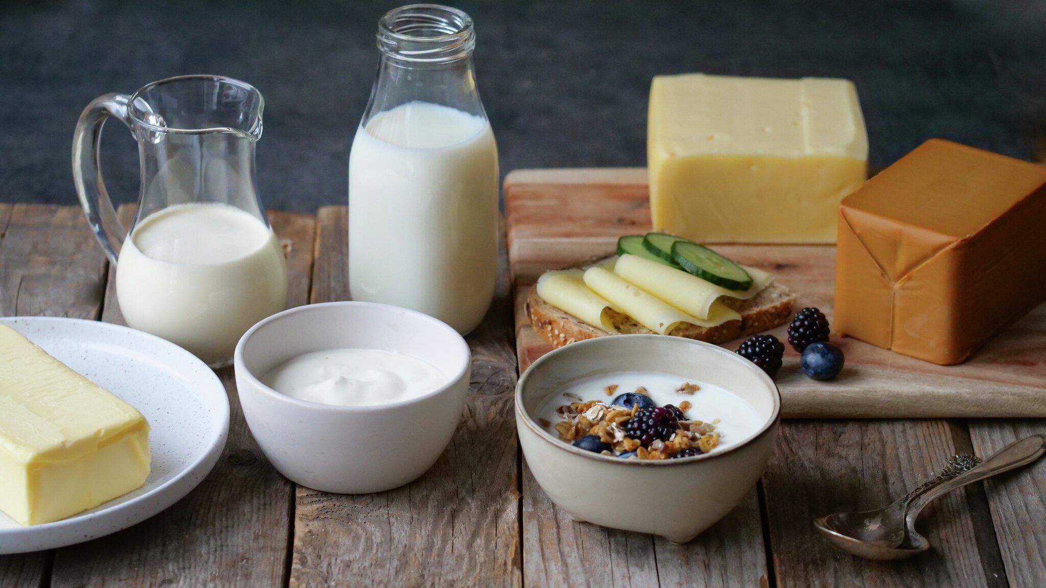Various dairy products including milk, butter, cheeses, and yogurt topped with granola and berries, arranged on a wooden table.
