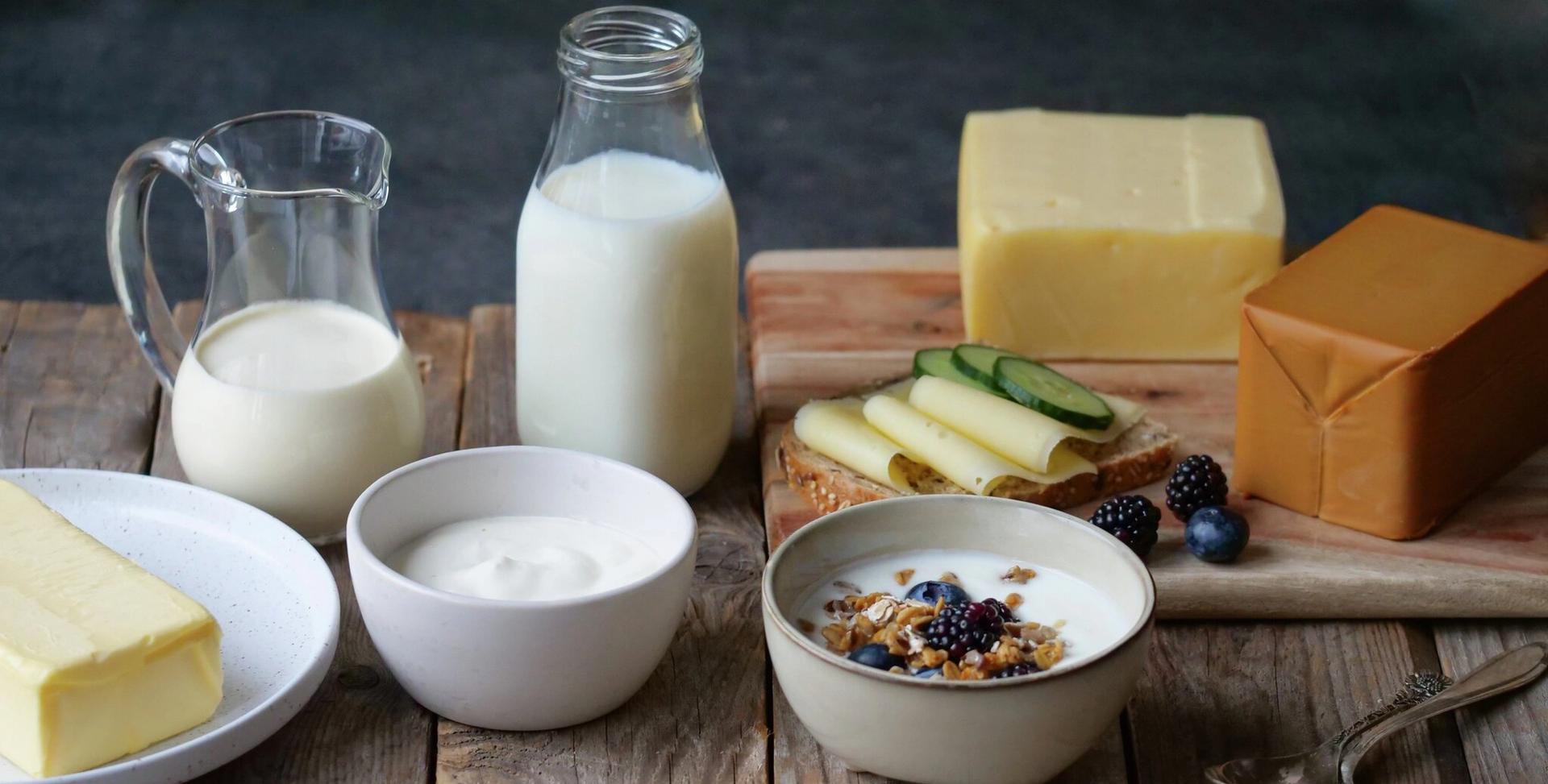 Various dairy products including milk, butter, cheeses, and yogurt topped with granola and berries, arranged on a wooden table.