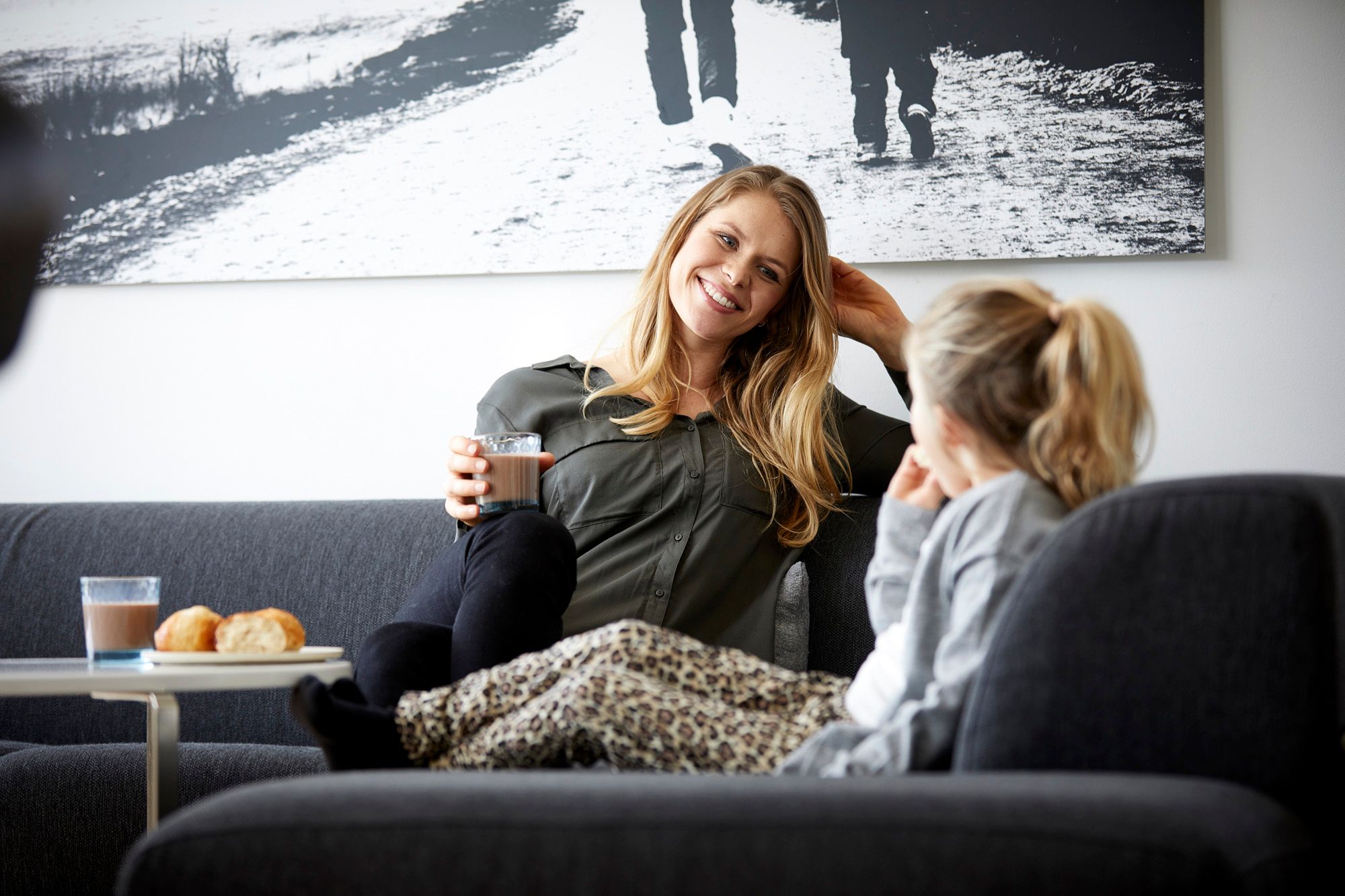 Mor med sjokolademelk og datter i sofa 