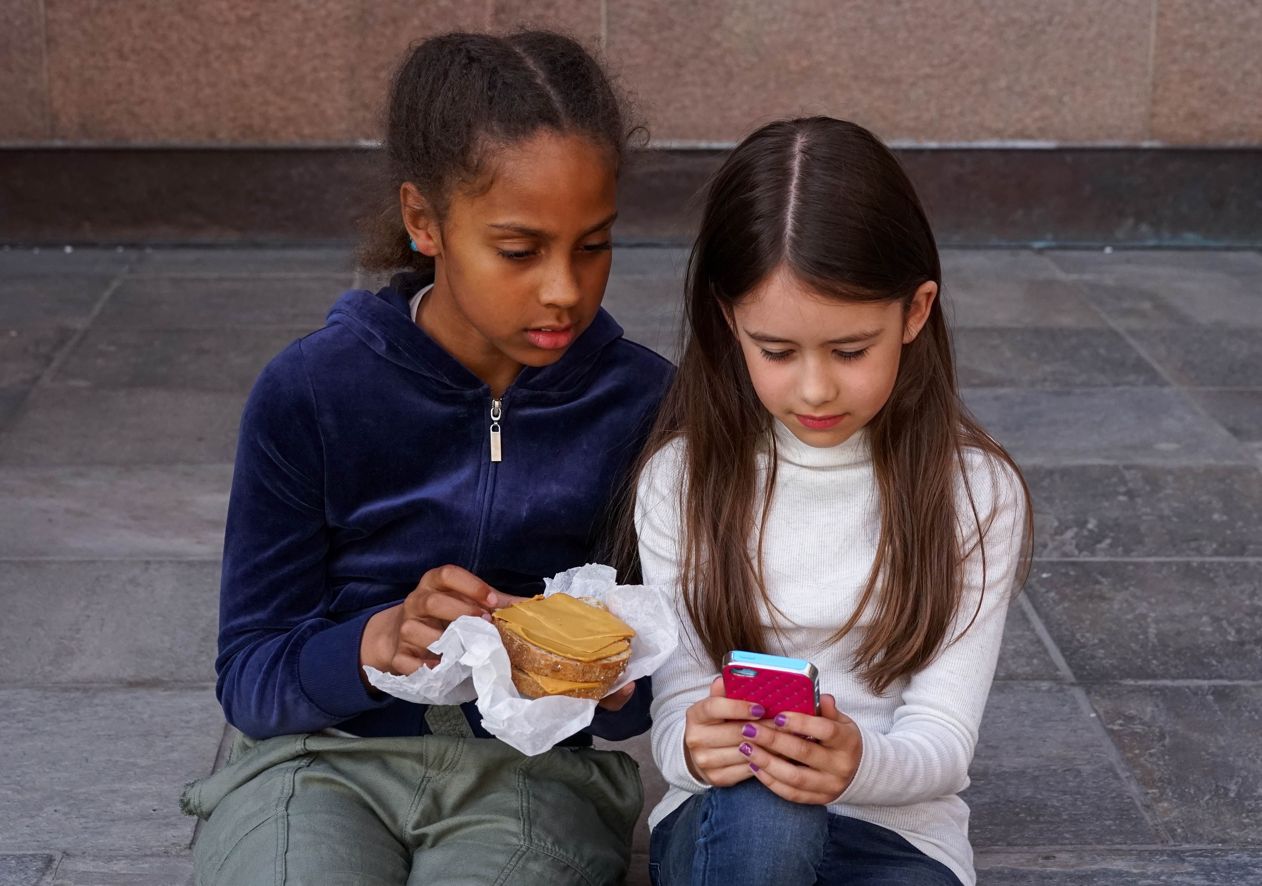 To jenter ser på mobil og spiser matpakke