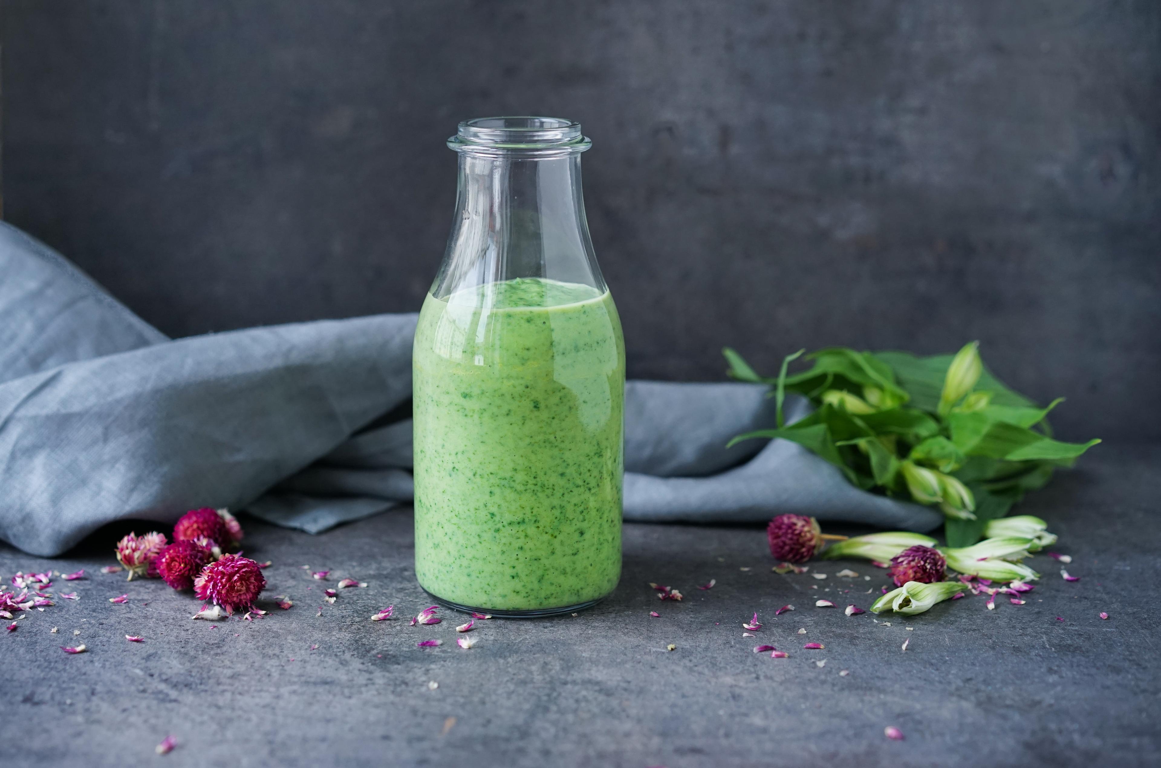 Glassflaske med grønn smoothie med spinat, avokado og yoghurt. Bak flasken ligger det en grå linserviett