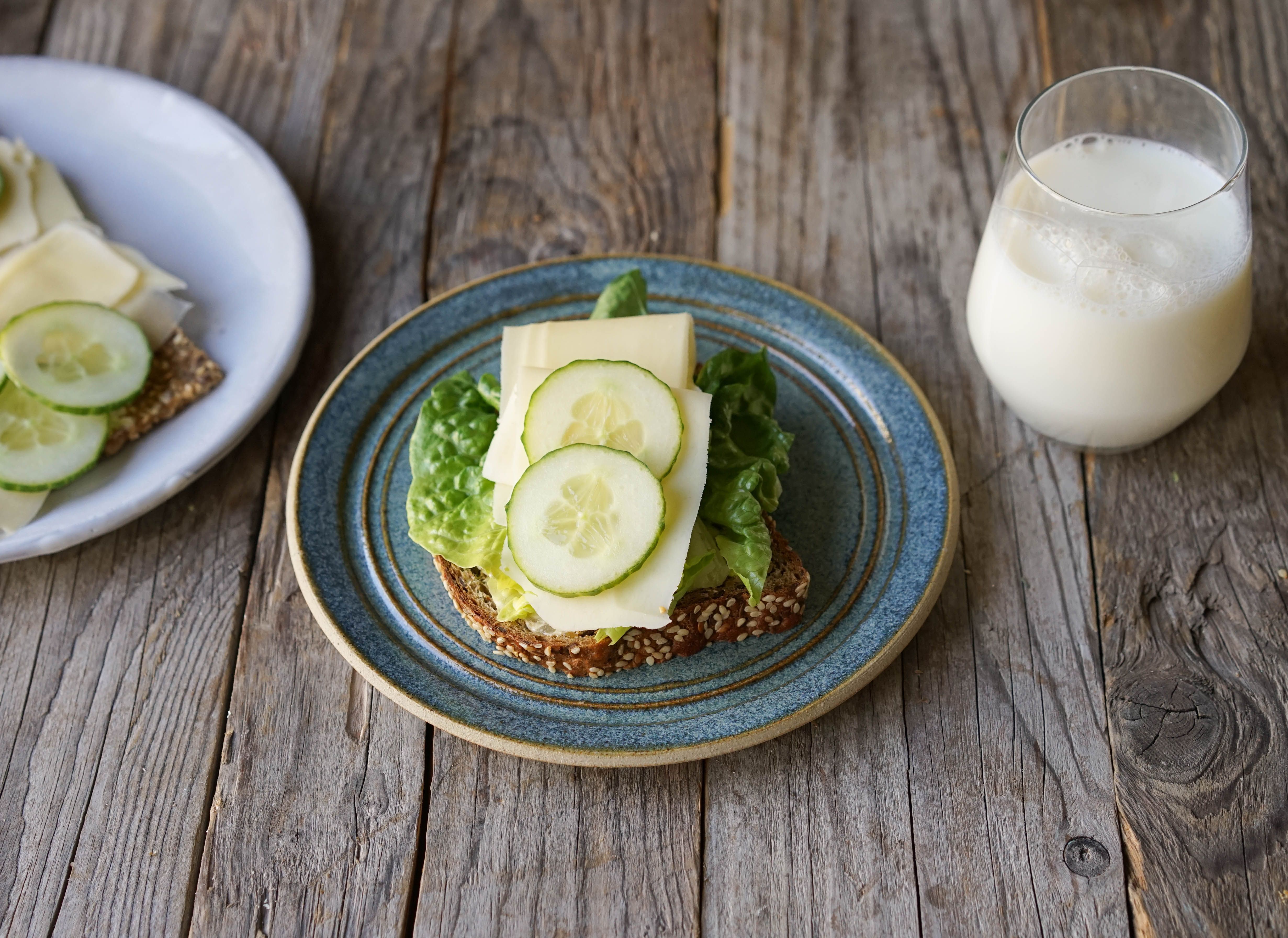 Blå tallerken med brødskive med salat og gulost og et glass melk