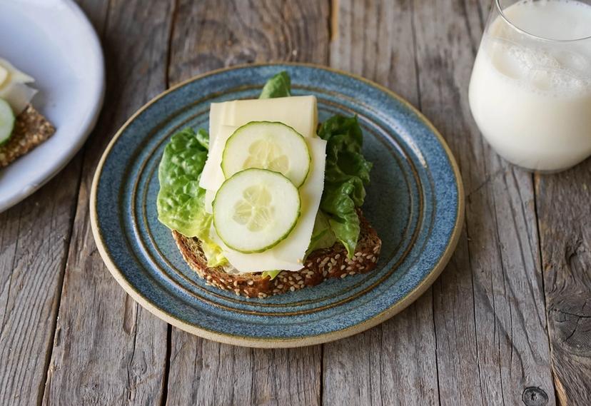 Blå tallerken med brødskive med salat og gulost og et glass melk