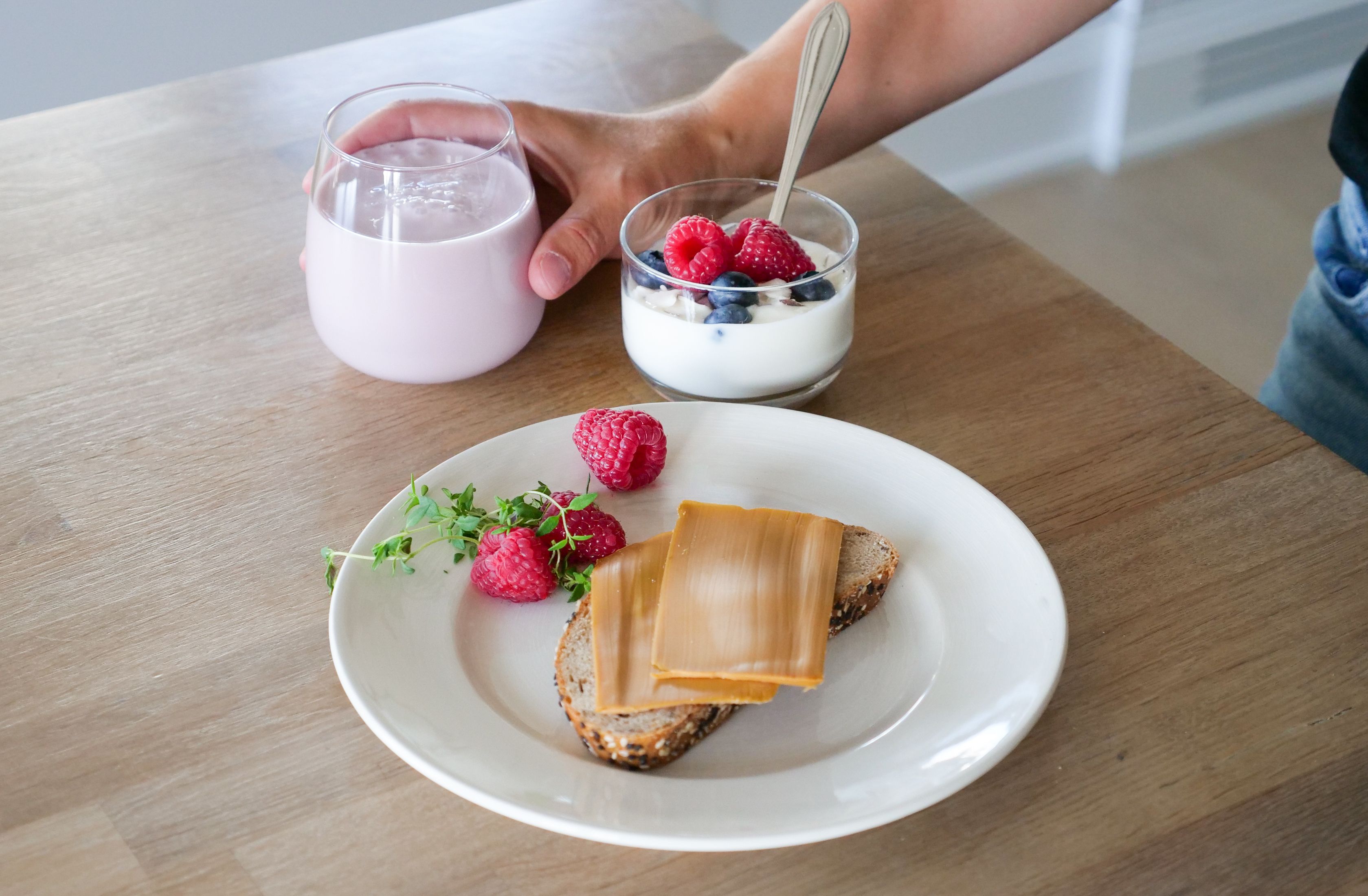 a person is holding a glass of milk next to a plate of food on a table .