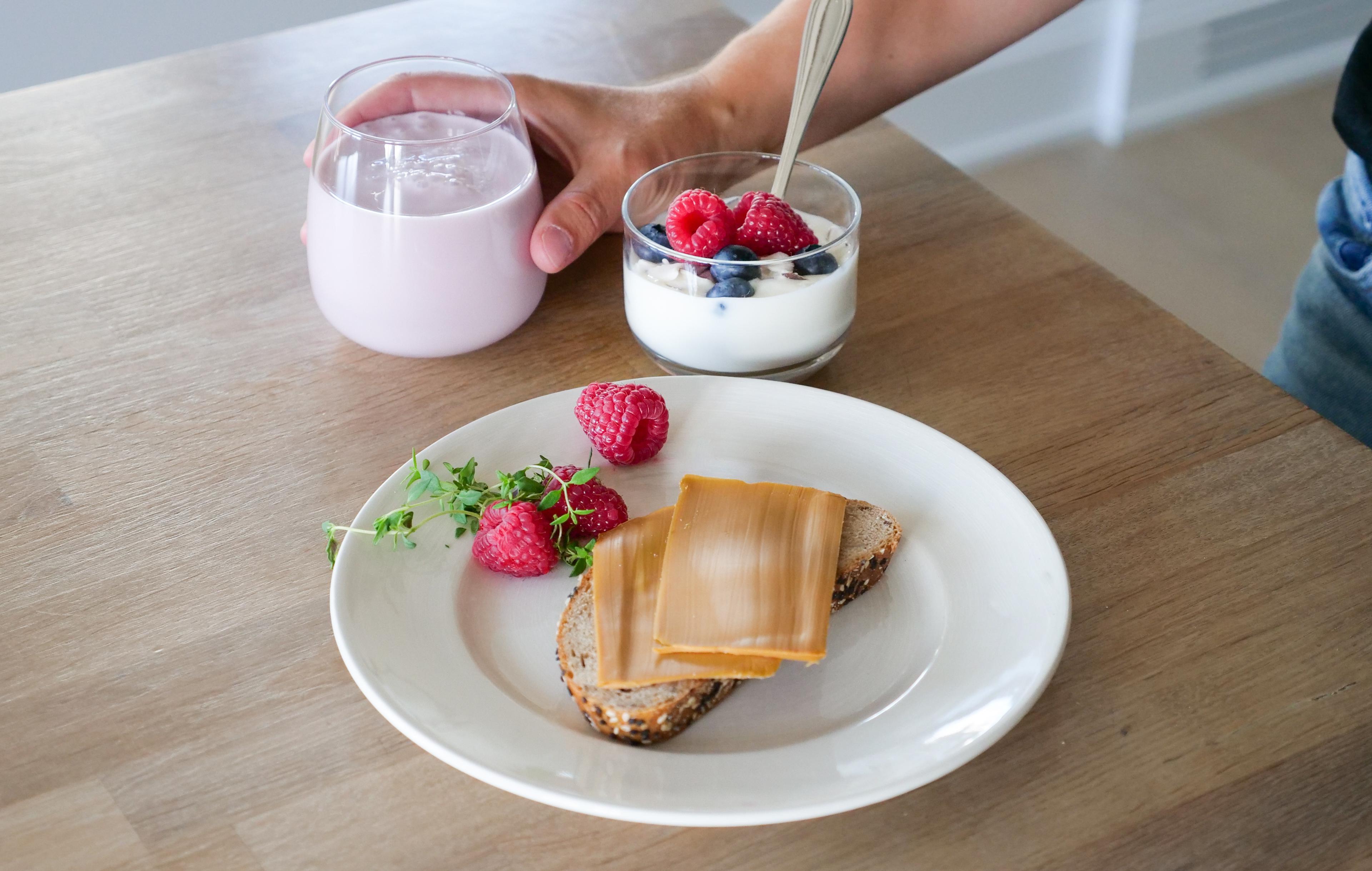 a person is holding a glass of milk next to a plate of food on a table .