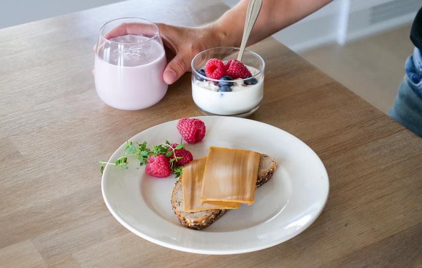 a person is holding a glass of milk next to a plate of food on a table .