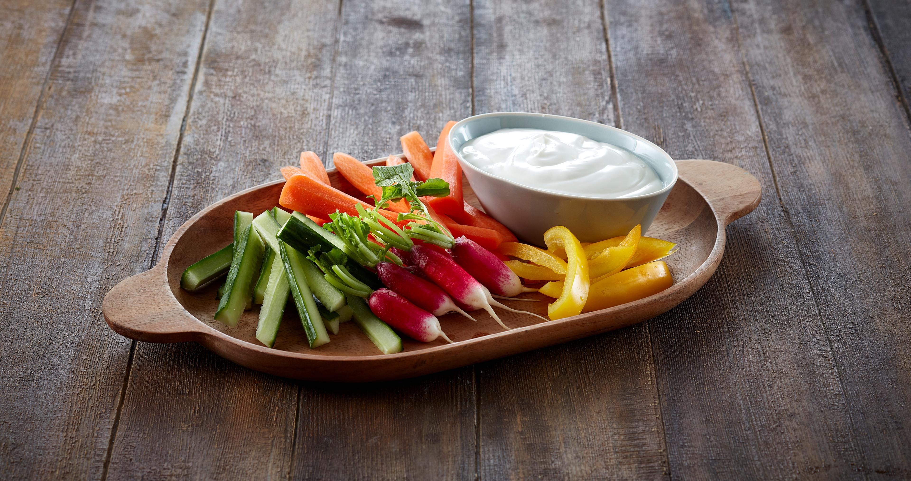 Trebrett med oppskjærte grønnskaer og en skål med lettrømme