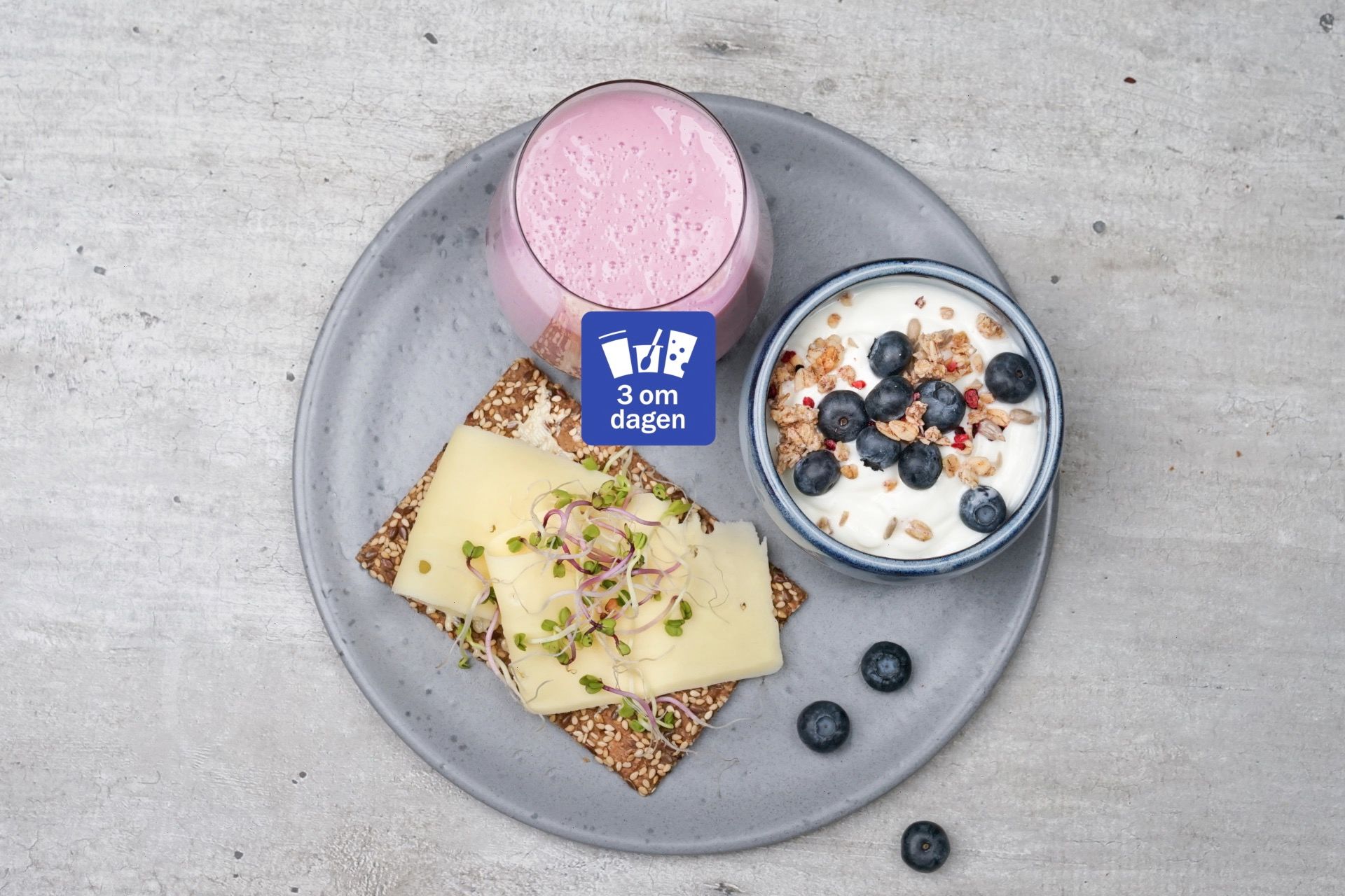 Knekkebrød med gulost og spirer, en skål med yoghurt, blåbær og musli og et glass syrnet melk