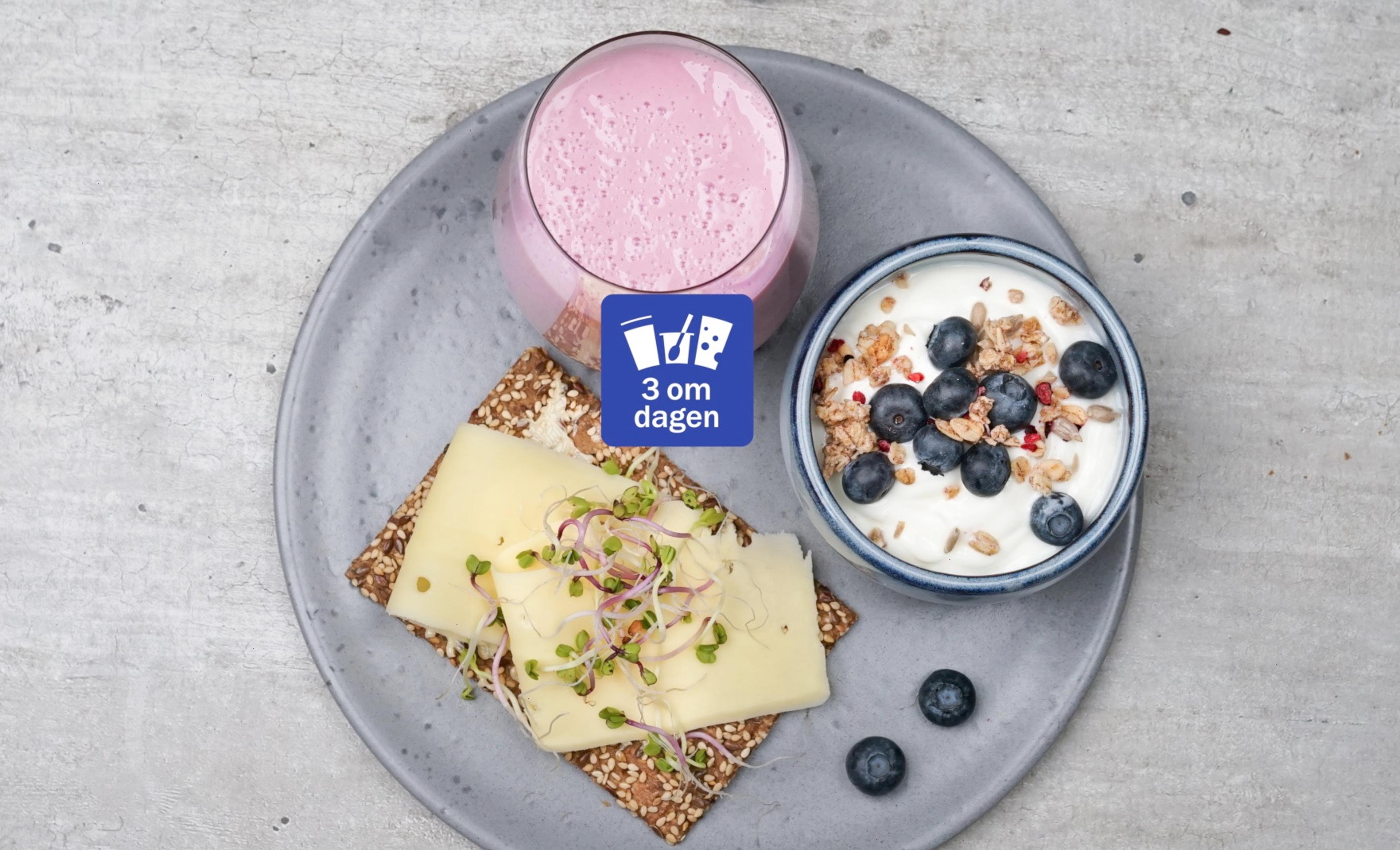 Knekkebrød med gulost og spirer, en skål med yoghurt, blåbær og musli og et glass syrnet melk